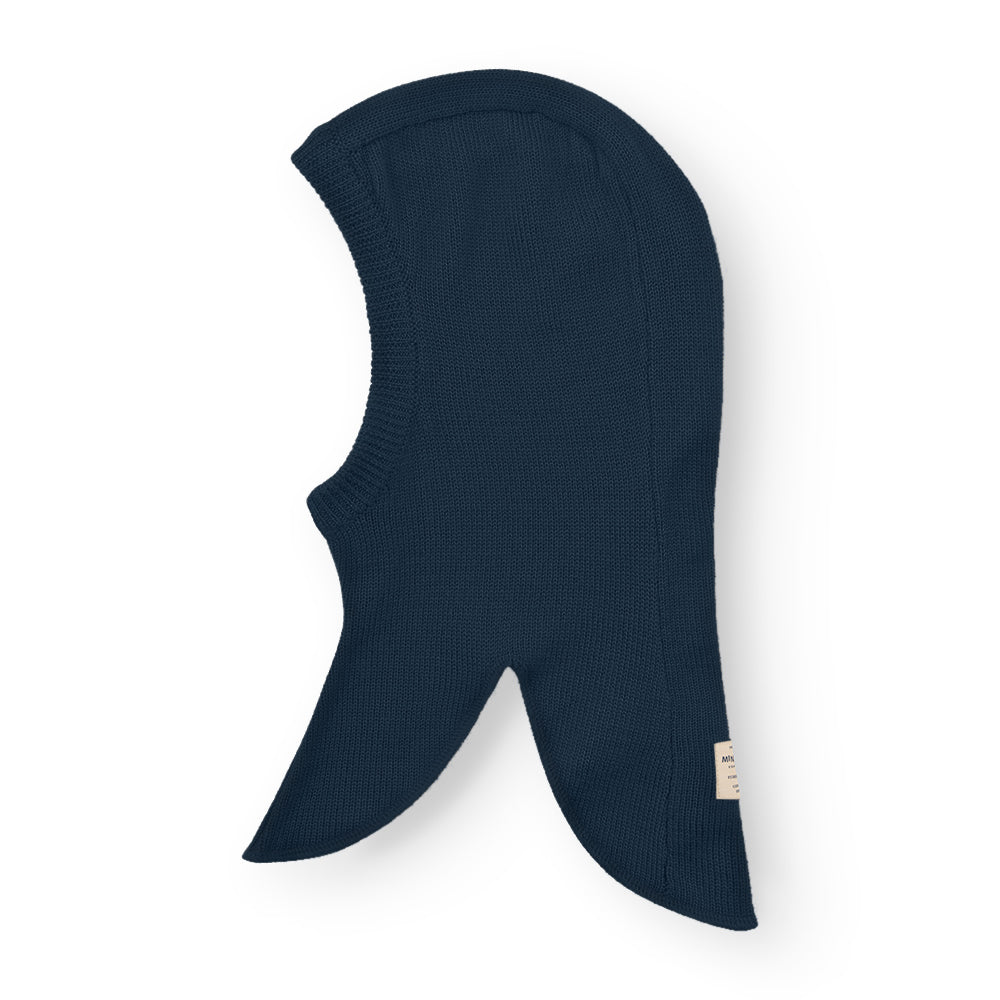 MATKEA light balaclava in navy blue merino wool, laid flat to showcase the seamless knitted construction with pronounced shoulder flaps and a shaped face opening for layering beneath helmets or winter hoods.