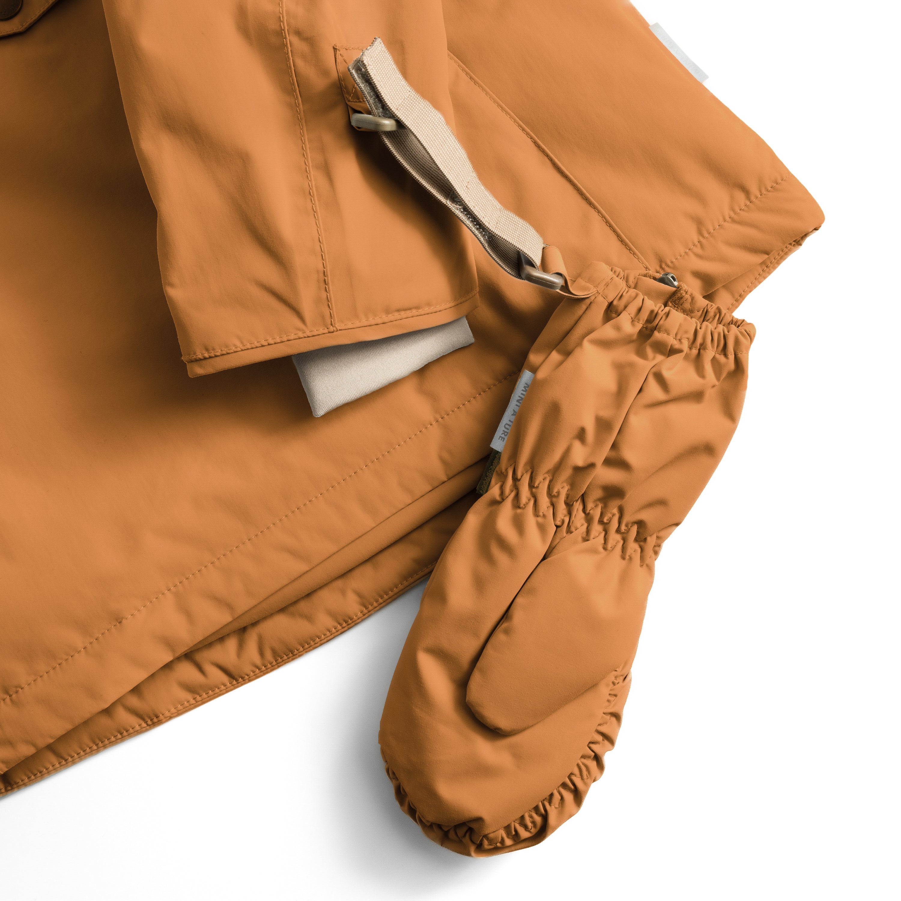 MATCESAR waterproof mitten in warm caramel brown shown with the front zip partially open to reveal the soft fleece lining, elastic gathered cuff with MINI A TURE branding, and beige webbing strap with D-ring attachment, displayed alongside matching jacket sleeve against a white background.