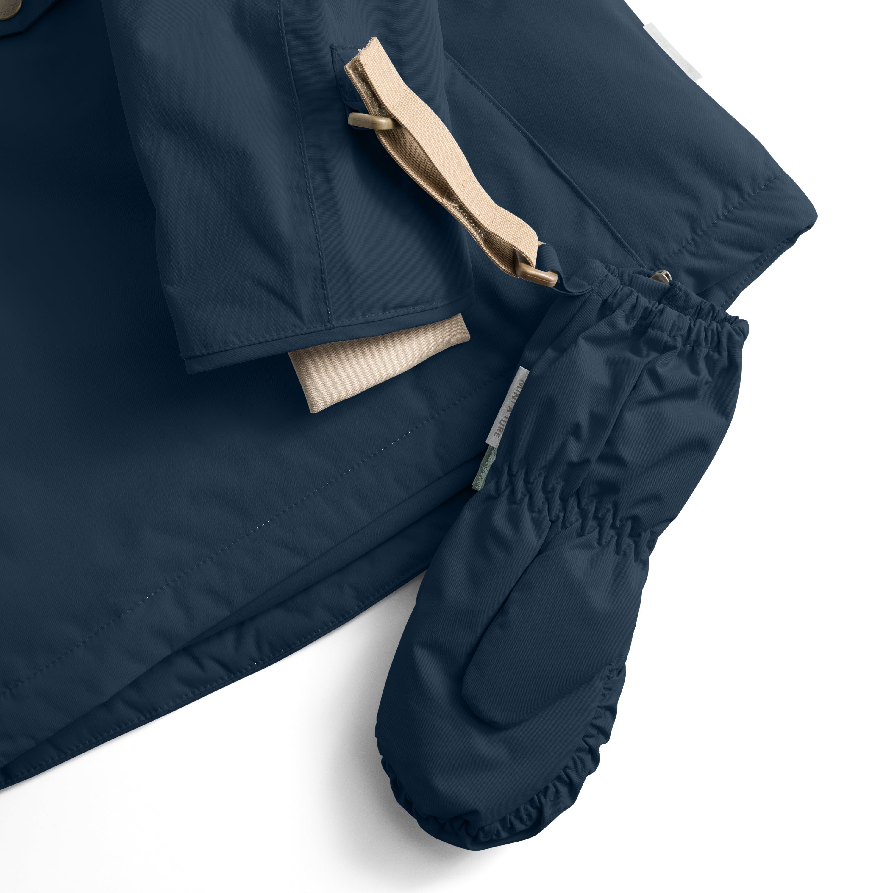 MATCESAR mitten in deep navy shown threaded onto a matching jacket sleeve via the beige webbing strap, with the elastic gathered cuff and fleece lining visible at the opening, demonstrating the attachment system that keeps mittens secured to MINI A TURE outerwear during wear.