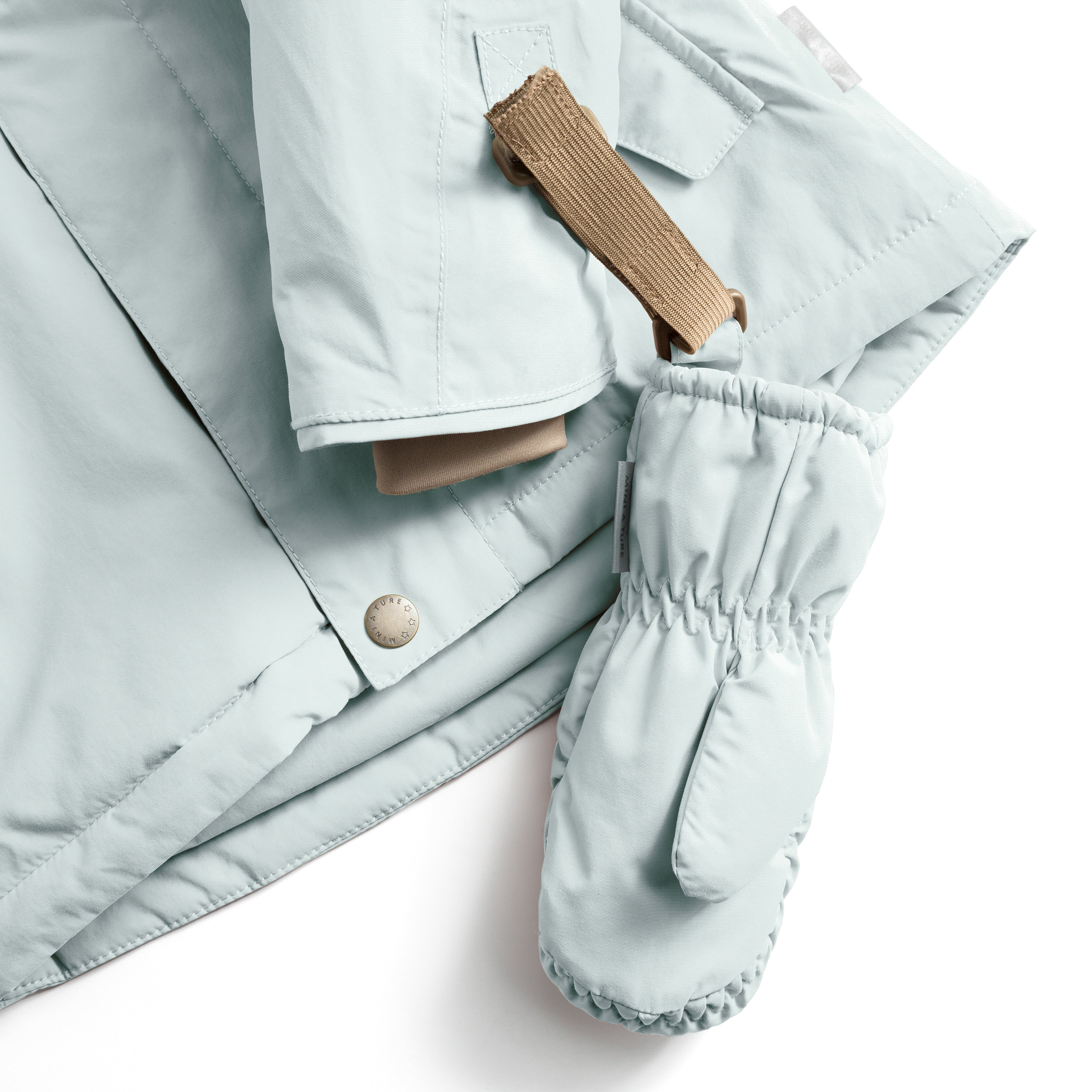 MATCORDT fleece lined mittens in pale blue shown attached to a matching jacket via the beige velcro strap and D-loop fastening, with the elastic gathered cuff and waterproof recycled polyamide shell visible alongside the jacket's press-stud closure and taped seam construction.