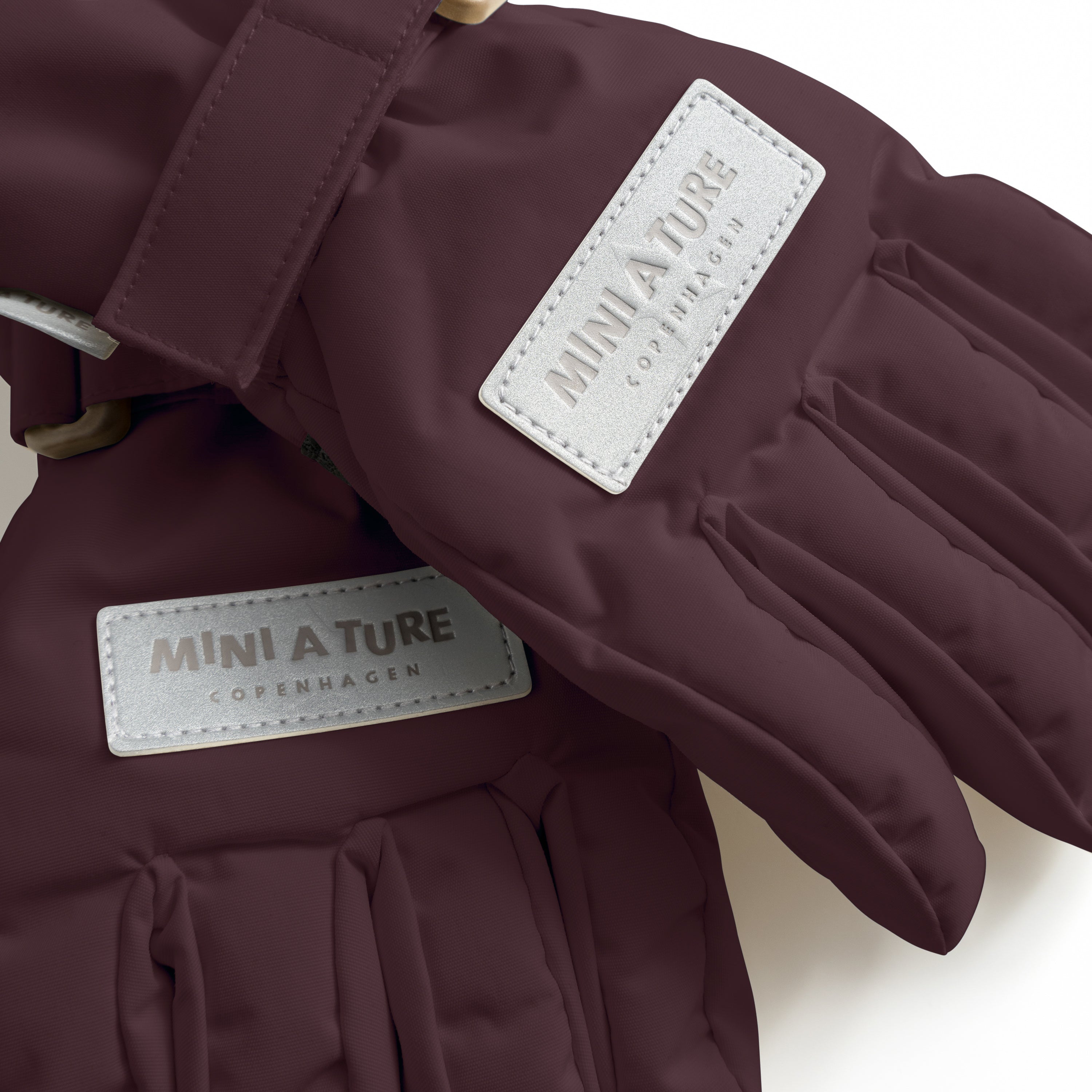 MATCELIO gloves in deep burgundy with embossed MINI A TURE Copenhagen labels on both the back of hand and extended cuff, photographed flat to show the waterproof recycled nylon outer shell, THERMOLITE padding construction and adjustable wrist strap with buckle closure.