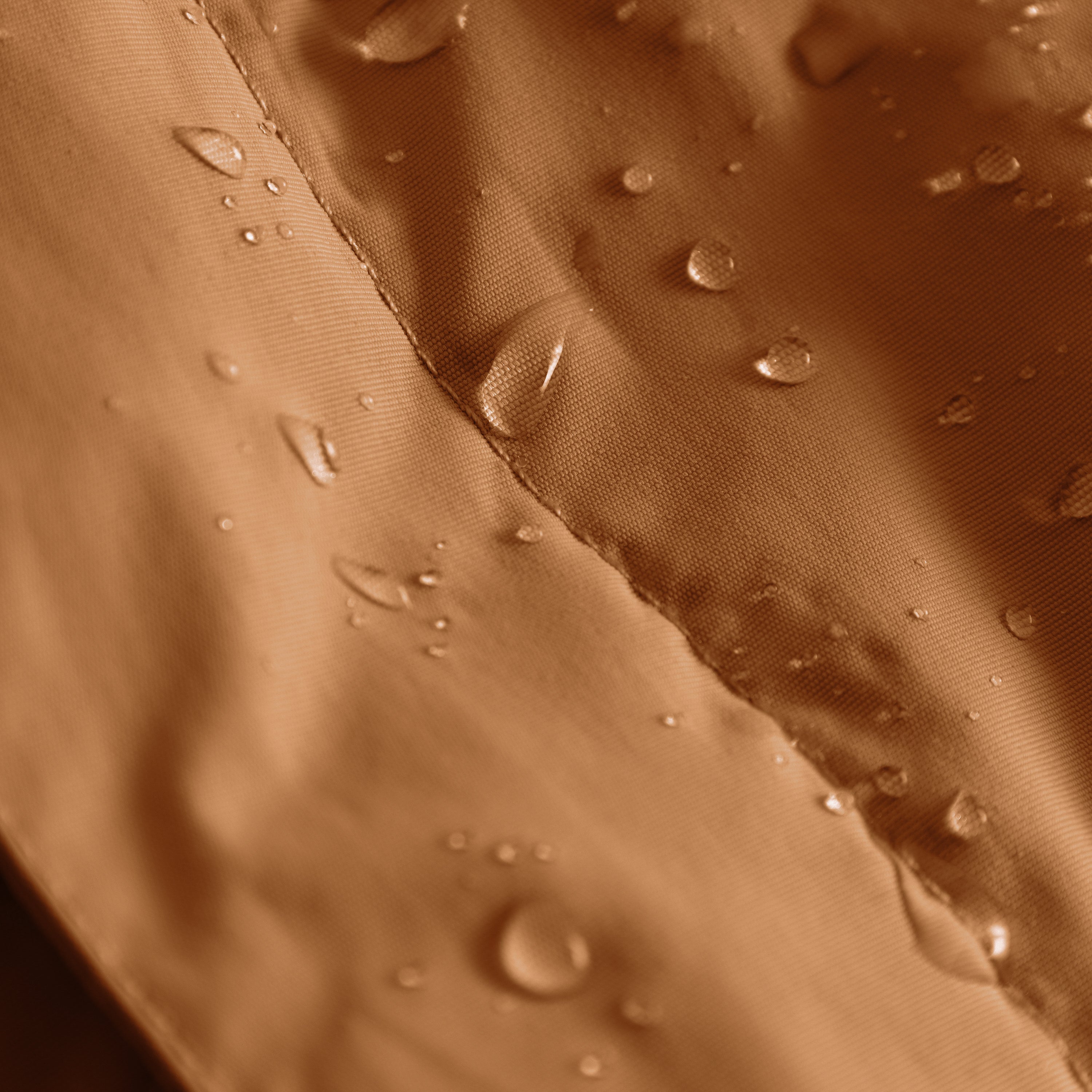 MATBABYWEN anorak in warm caramel brown showing water droplets beading on the recycled polyamide outer shell treated with fluorine-free Bionic Finish Eco, with a close view of the fully taped seam construction that provides genuine waterproofing across the 12,000mm rated fabric.