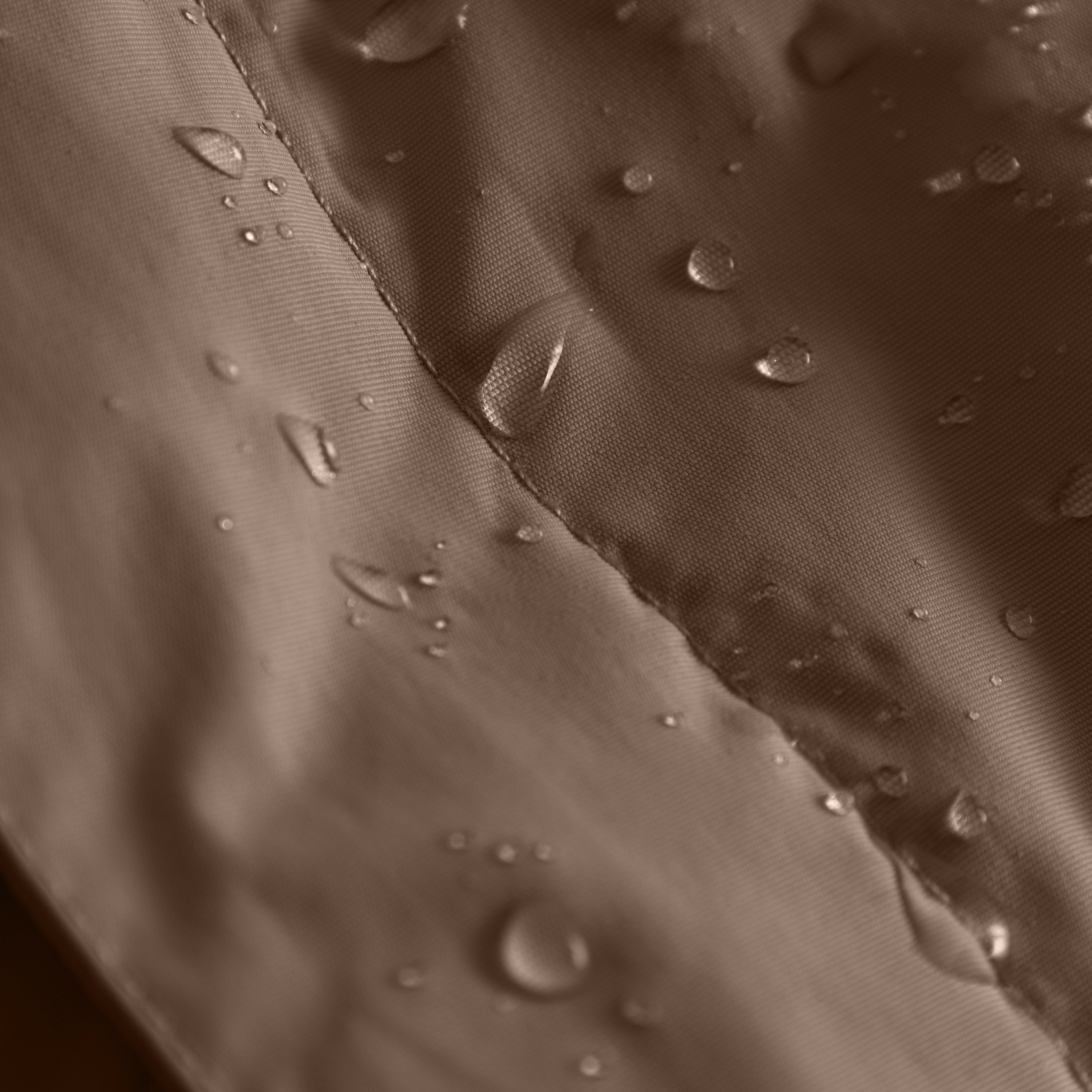 Close-up of the MATBABYWEN anorak in brown showing water droplets beading on the recycled polyamide outer shell treated with fluorine-free Bionic Finish Eco, with a detailed view of the taped seam running diagonally across the waterproof fabric.