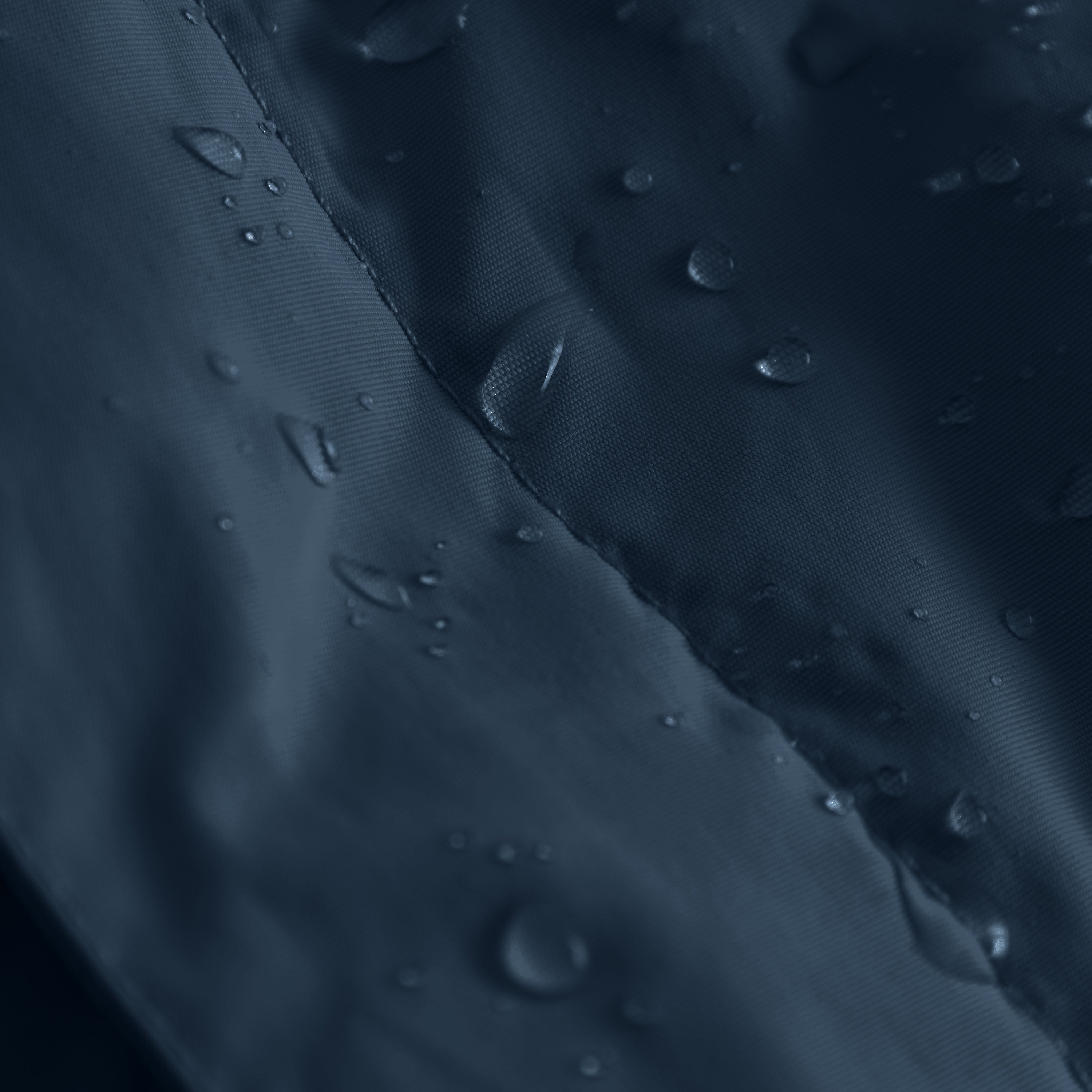 Close-up of the MATBABYWEN anorak in navy blue showing water droplets beading on the recycled polyamide outer shell treated with fluorine-free Bionic Finish Eco, with a detailed view of the taped seam running diagonally across the waterproof fabric.