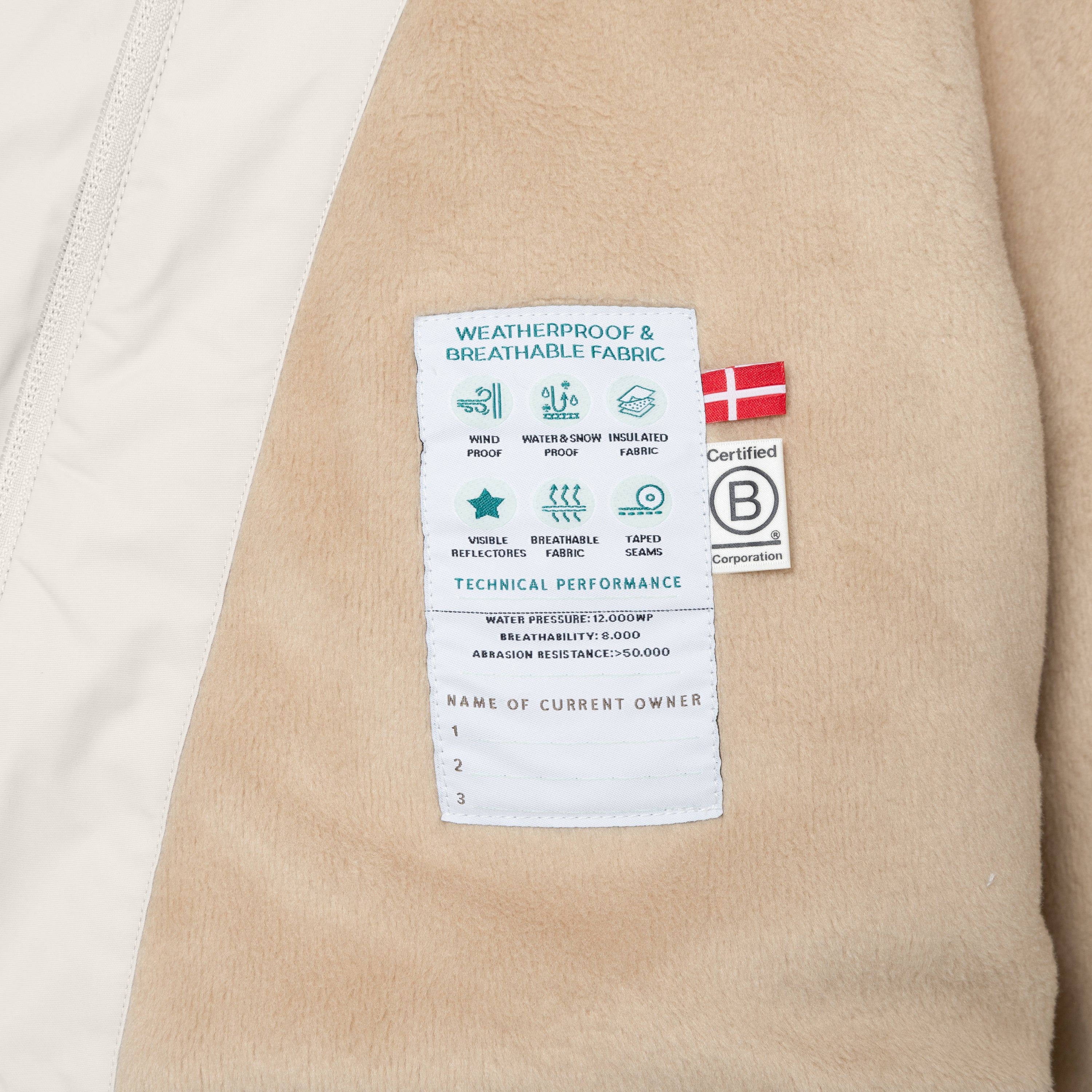 Interior care label of the MATWANG fleece-lined winter jacket sewn onto beige fleece lining, displaying weatherproof and breathable fabric icons, technical performance ratings including 12,000mm water pressure, 8,000 breathability and abrasion resistance above 50,000, Danish flag, B Corp certification logo, and owner registration section with numbered lines.