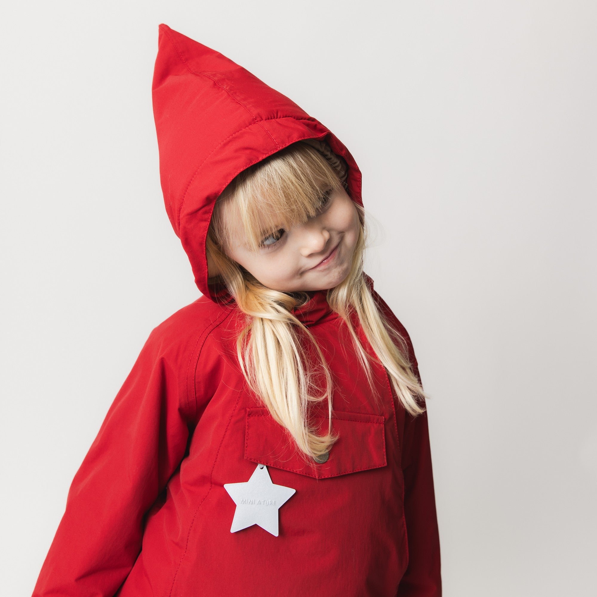 Young child wearing the MATWANG fleece-lined winter jacket in bright red with a pointed hood, showing the white reflective star detail on the chest pocket and the waterproof recycled nylon shell.