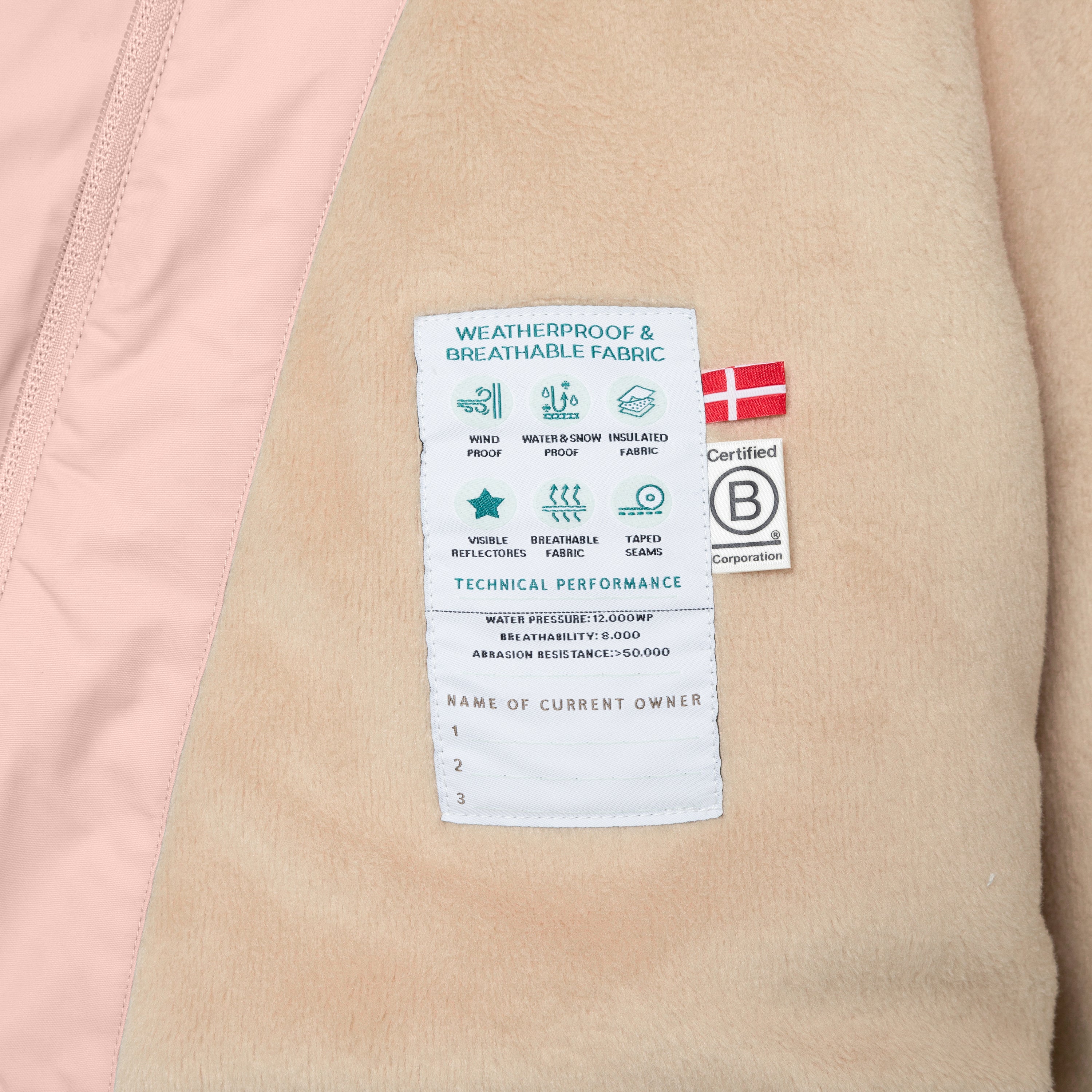 Interior label of MATWANG fleece-lined winter jacket showing technical performance specifications including 12,000mm waterproof rating, 8,000 breathability, taped seams, and B Corp certification, with soft beige fleece lining and pink outer shell visible.