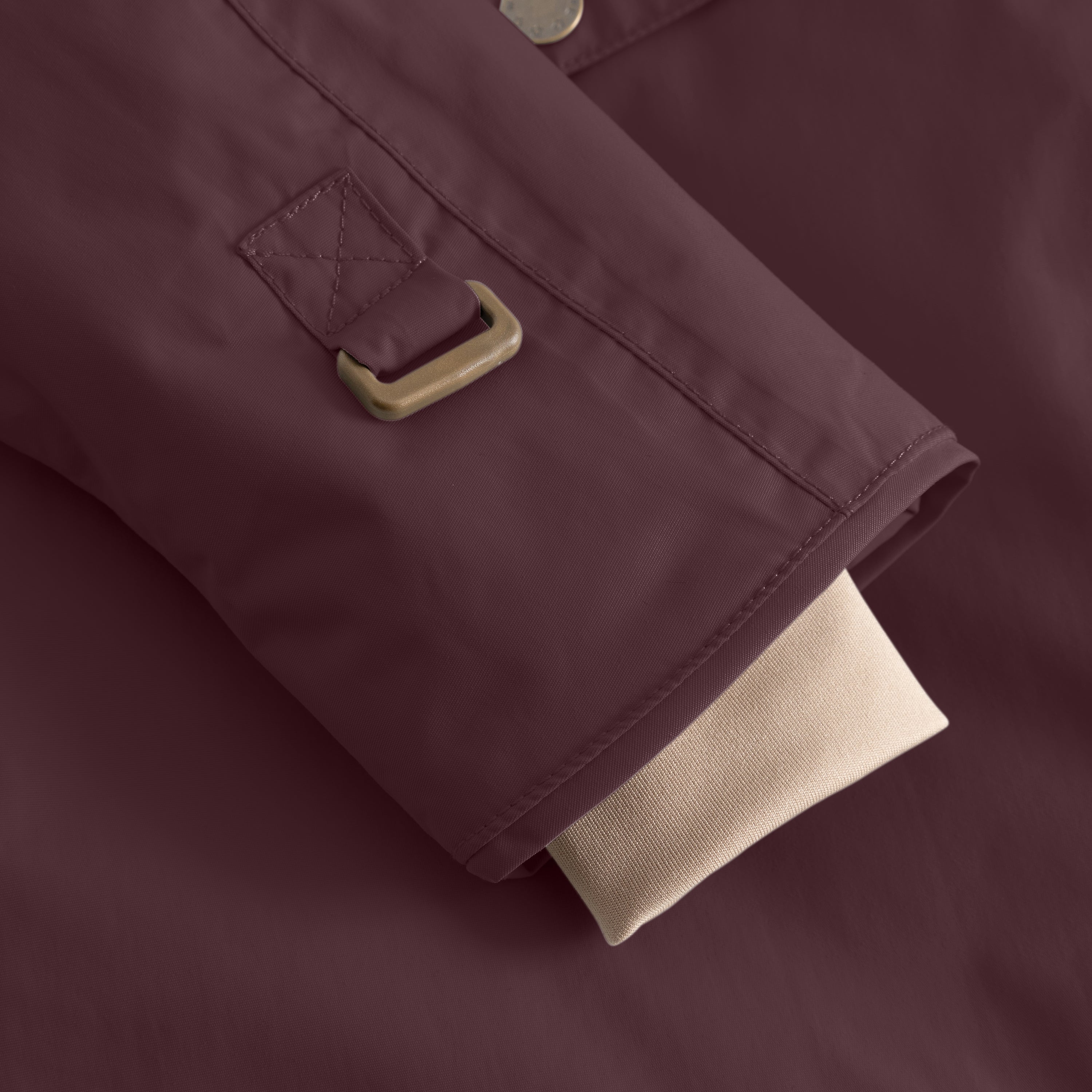 Detail of the MATWANG fleece-lined winter jacket's adjustable internal waist strap with a bronze-toned metal buckle and quilted fabric tab featuring cross-stitch detailing, positioned above the beige ribbed knit cuff on the deep burgundy waterproof recycled nylon shell.