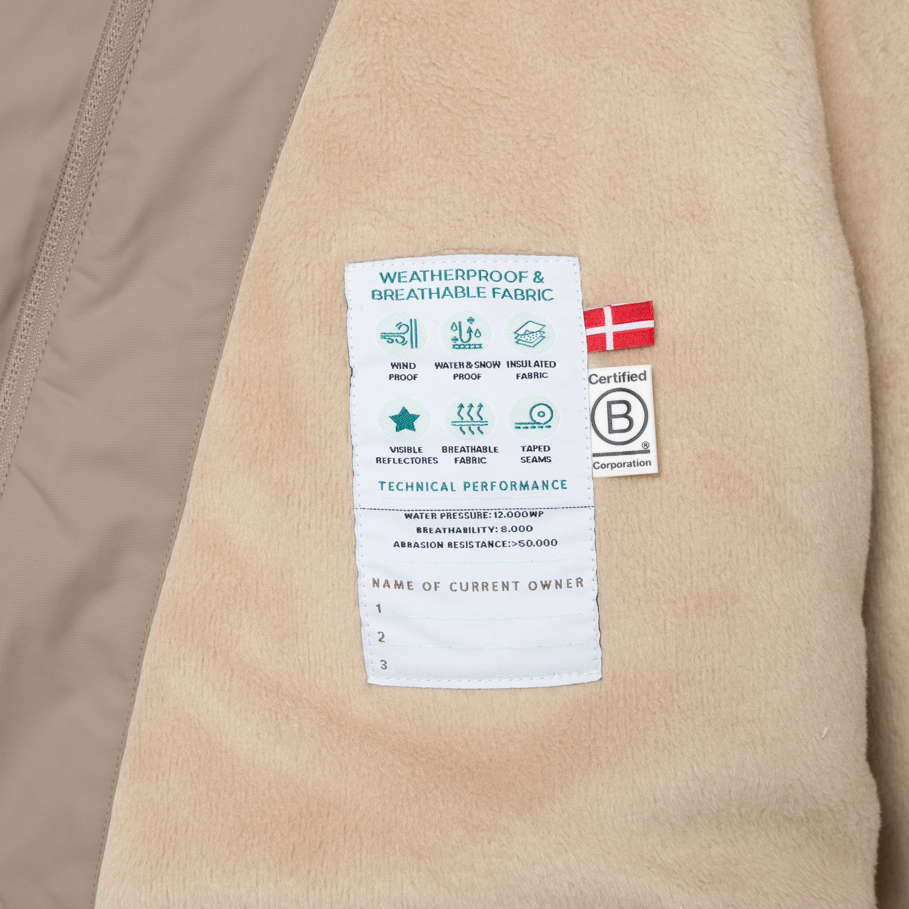 Fleece-lined kids' winter jacket interior showing technical performance label with waterproof rating, breathability specification, taped seams icon and B Corp certification badge on soft beige lining.
