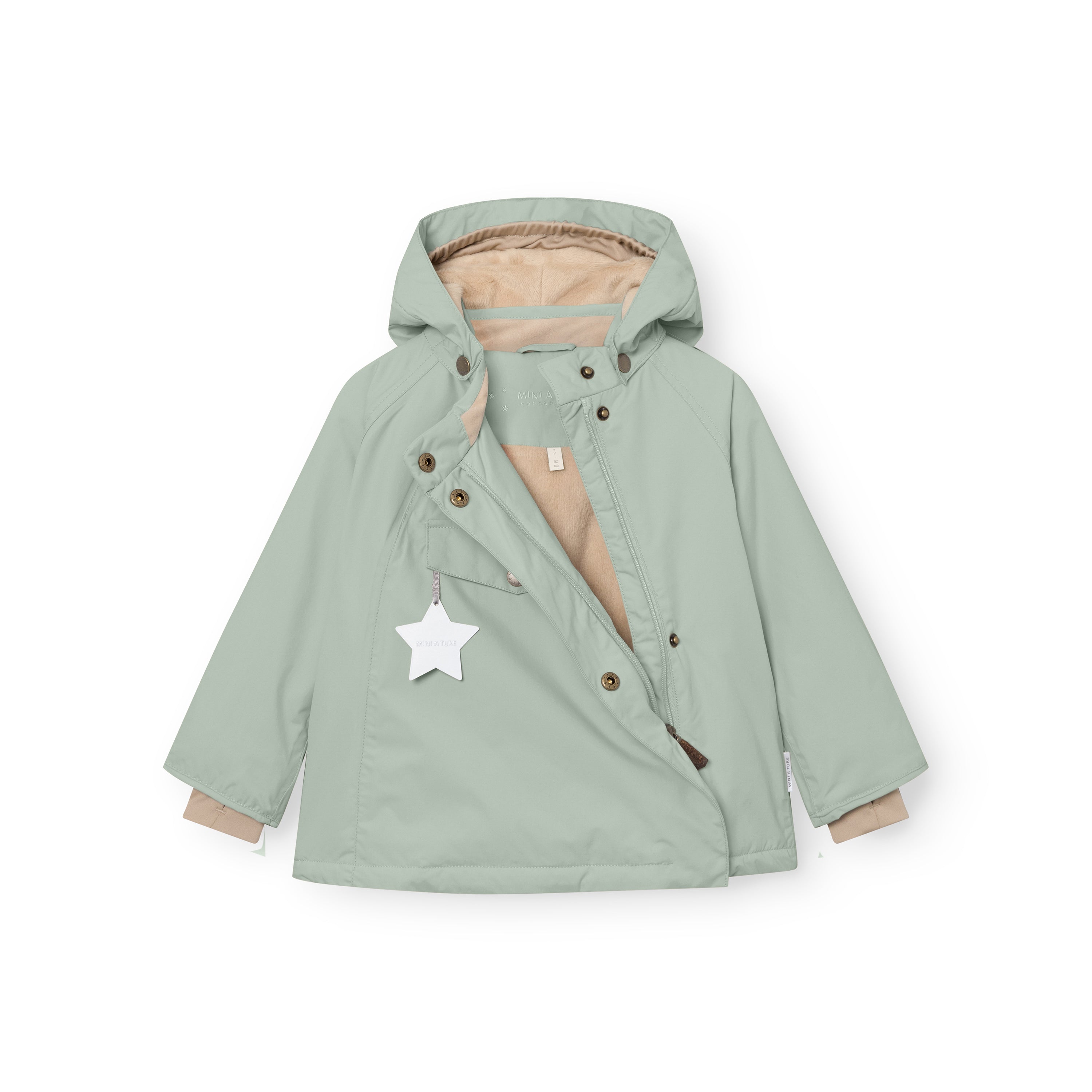 MATWANG fleece-lined winter jacket in soft sage green displayed flat with the concealed slanted zip fully open, showing the beige fleece lining throughout the interior, bronze press-stud fastenings along the zip placket, detachable pointed hood, white reflective star hanging from the chest pocket, and bronze D-ring buckles at the cuffs.