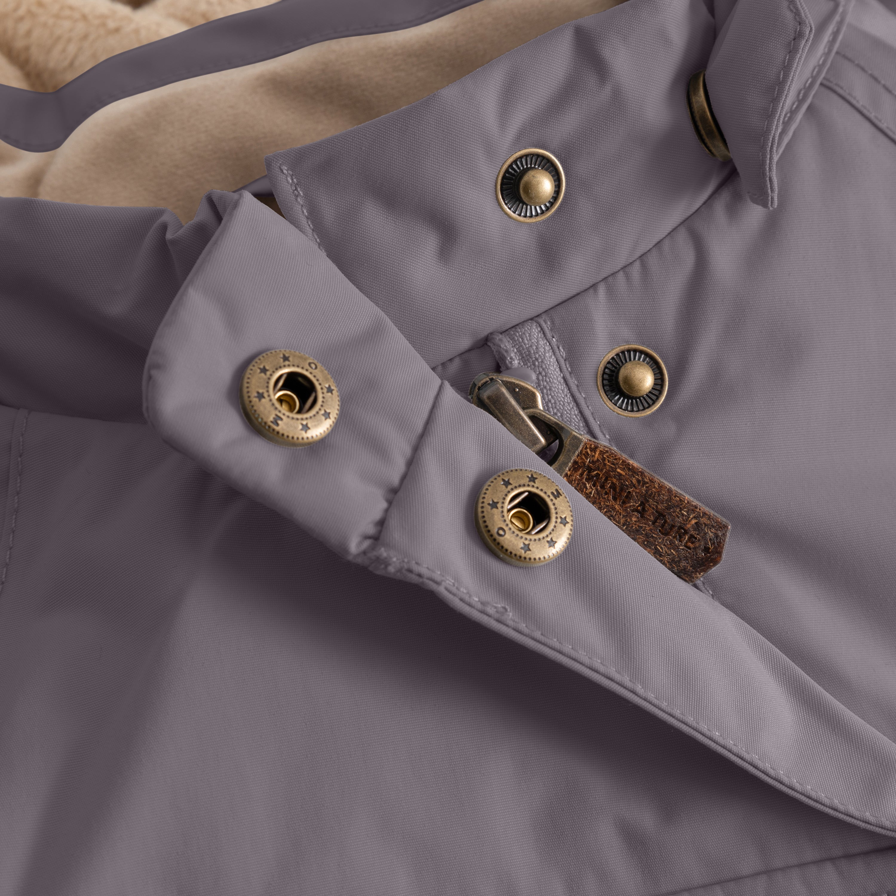 Close-up of the MATWANG fleece-lined winter jacket's detachable pointed hood showing bronze-toned press-stud fastenings on the grey waterproof recycled nylon shell, with a brown fabric zip pull and beige fleece lining visible at the hood edge.