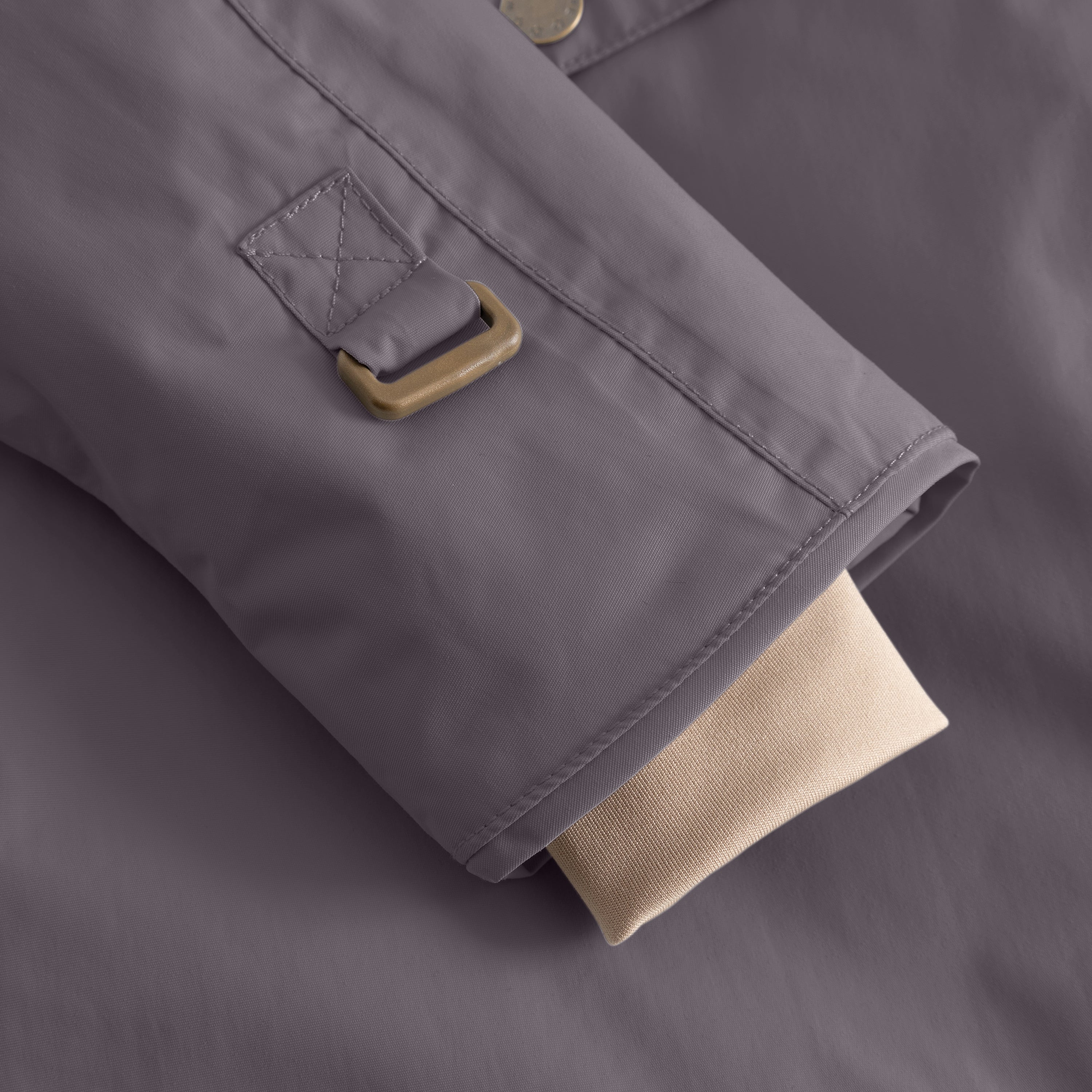 Detail of the MATWANG fleece-lined winter jacket's sleeve hem showing the bronze-toned metal D-ring attachment point with a quilted fabric loop featuring cross-stitch detailing, alongside the beige ribbed knit snow cuff extending from beneath the grey waterproof recycled nylon shell.