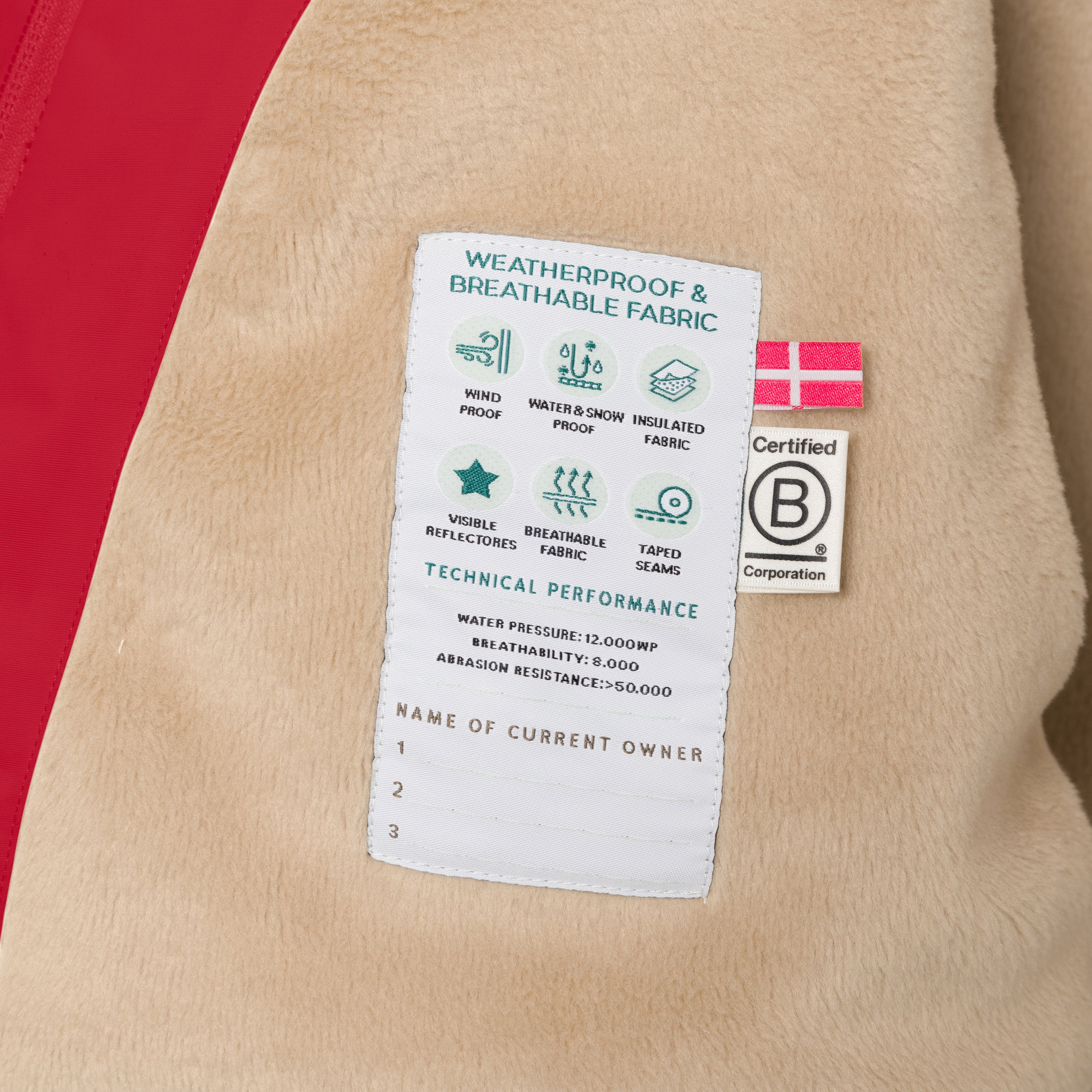Detail of the MATWANG fleece lined winter jacket's internal technical label sewn into the beige fleece lining, showing windproof, waterproof and breathable fabric icons, 12,000mm water pressure rating, 8,000 g/m²/24h breathability, 50,000+ Martindale abrasion resistance, Danish flag, B Corp certification logo, and numbered spaces for recording current owner details.