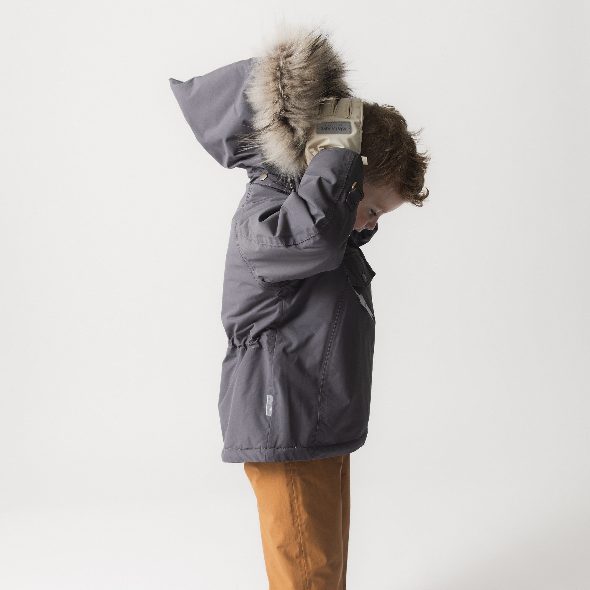 Child pulling the MATWANG fleece lined winter jacket's detachable real fur hood over their head, demonstrating the adjustable fit and coverage provided by the hood with elastic-string adjustment and hidden zip fastening.