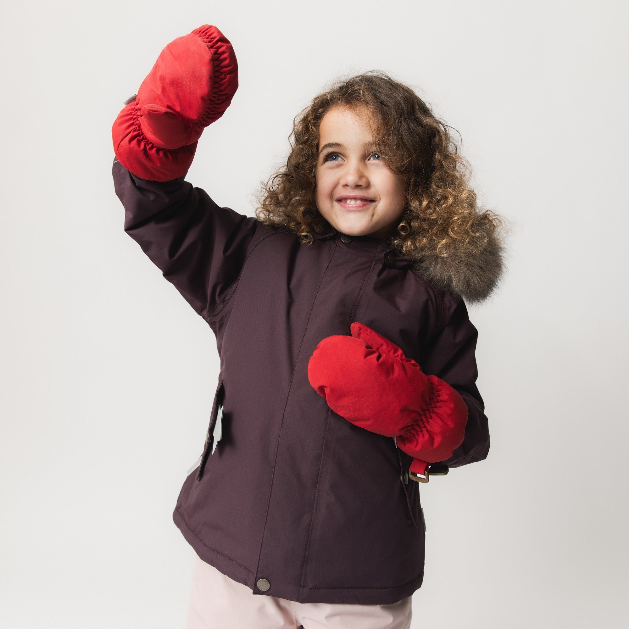 Young child wearing the MATWALLY fleece lined winter jacket in burgundy with detachable real fur hood trim and bright red mittens, demonstrating the jacket's freedom of movement during active play.