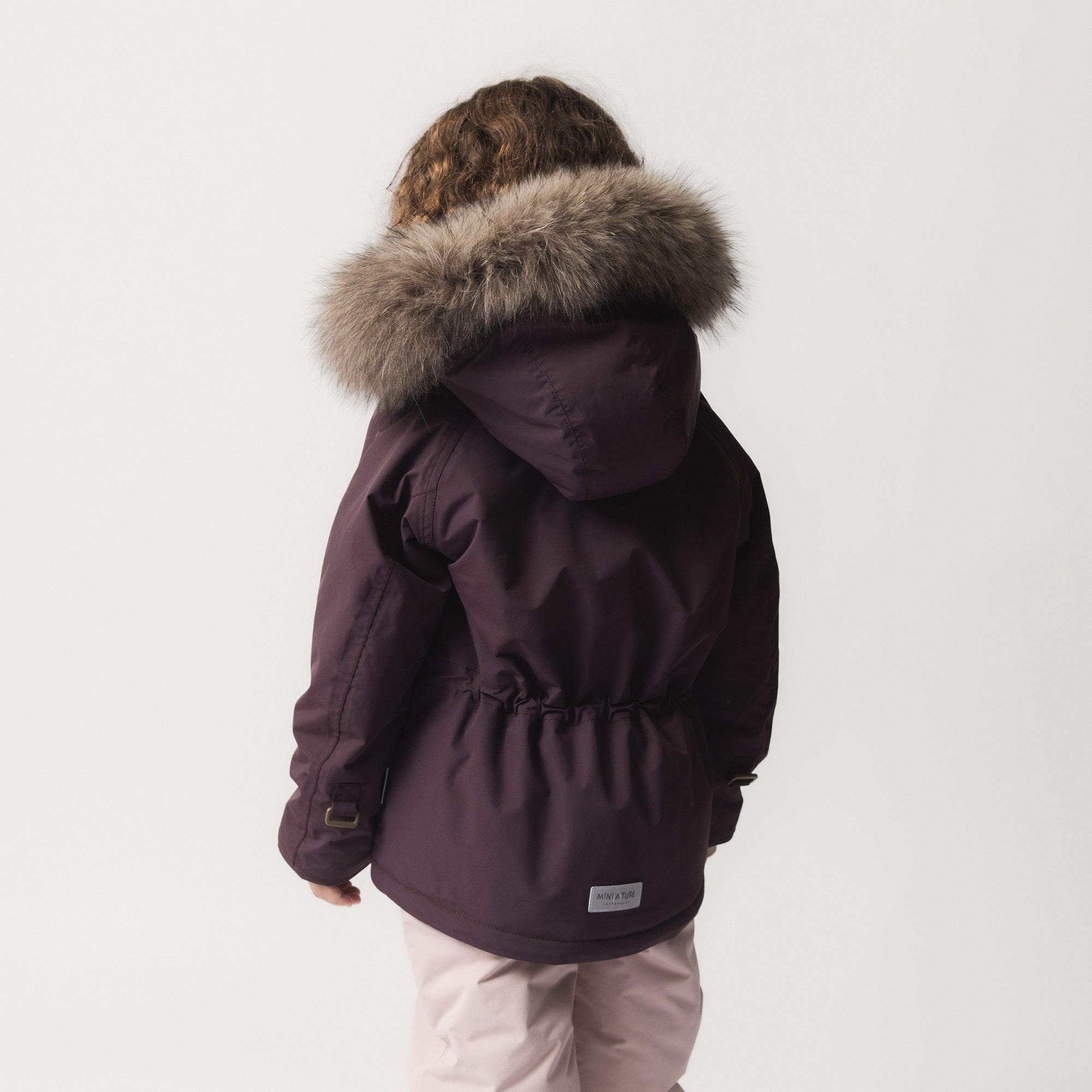 MATWALLY fleece lined winter jacket in deep burgundy shown from the side, highlighting the detachable real fur hood trim, adjustable internal waist with elastic drawstring, and the jacket's silhouette during movement.
