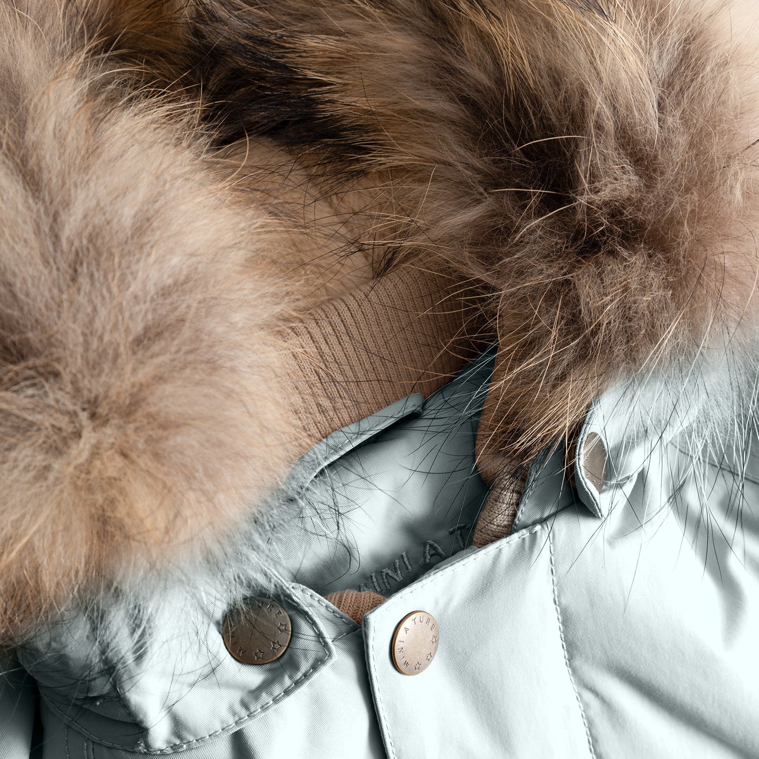 Close-up of the MATWALLY fleece lined winter jacket's hood attachment in soft pale blue, showing the hidden zip mechanism beneath the detachable real fur trim, with branded press studs securing the hood to the jacket's collar and the natural multi-tonal fur displaying its layered texture.