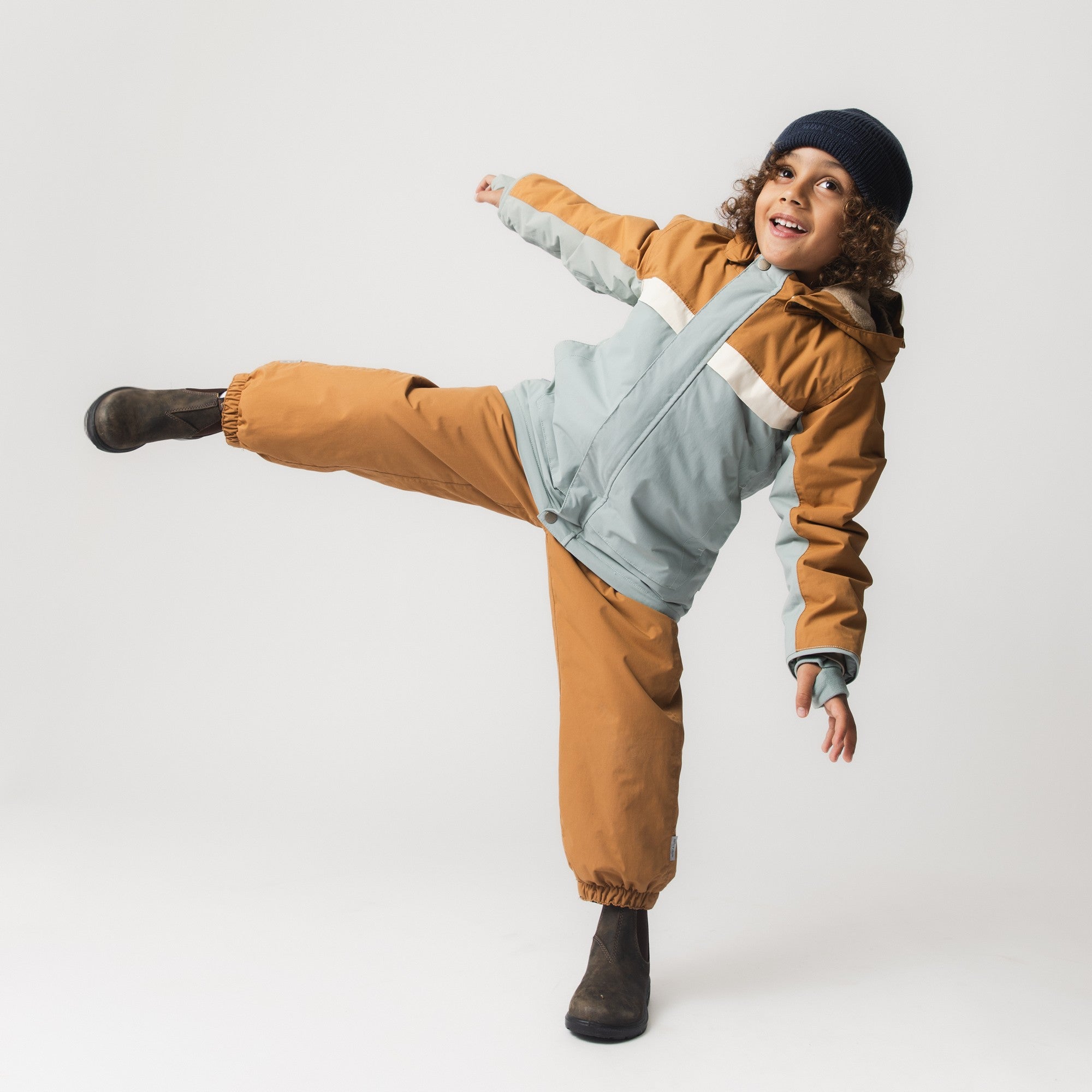 Young child wearing the MATWALDO fleece lined winter jacket in a colourblock design of brown sugar and baby blue, paired with matching waterproof trousers, demonstrating freedom of movement during active play.