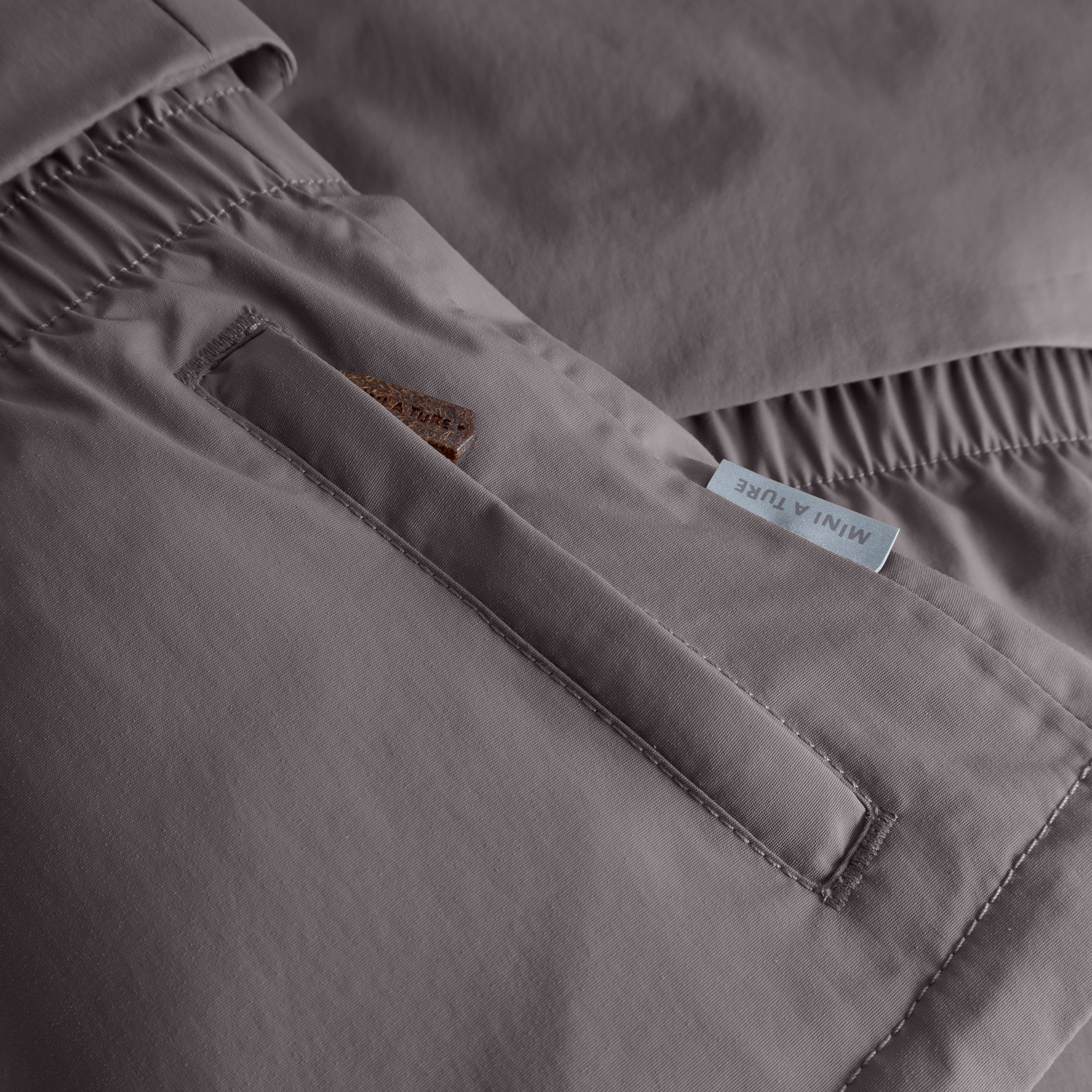 MATALGEANA winter jacket detail in grey showing the internal snow cuff with thumb opening at the sleeve, beige fleece lining at the cuff edge, elasticated waist panel with gathered stitching, and MINI A TURE woven label on the waterproof recycled polyamide shell.