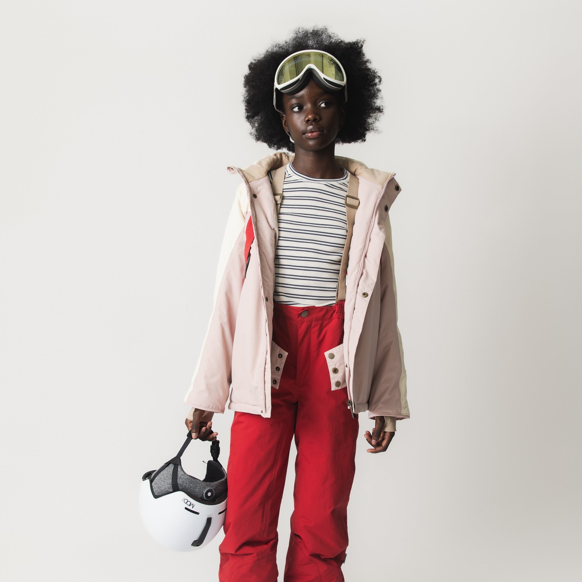 MATWITTE snow pants in bright red worn with ski goggles and a pale pink jacket, showing the full-length fit, elasticated ankle cuffs with foot straps, and the trousers' suitability for layering during skiing and winter activities.