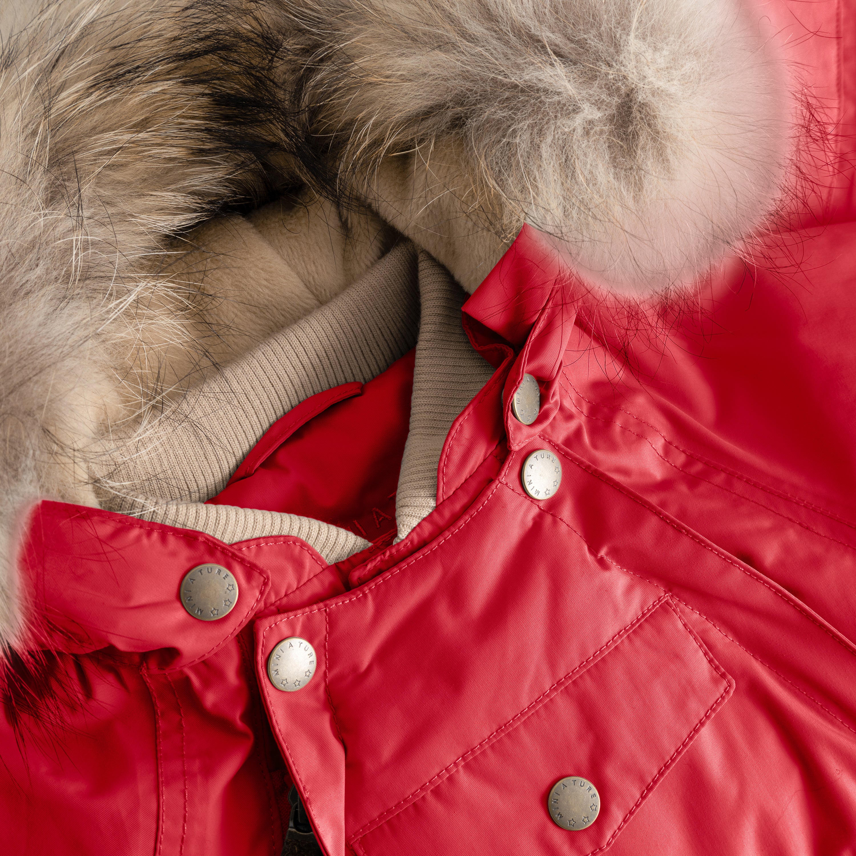 Close-up of MATWISTI fleece lined snowsuit fur in bright red showing the detachable genuine fur hood trim, beige ribbed collar, MINI A TURE branded press-stud fastenings along the chest, and front pocket detail on the waterproof shell.