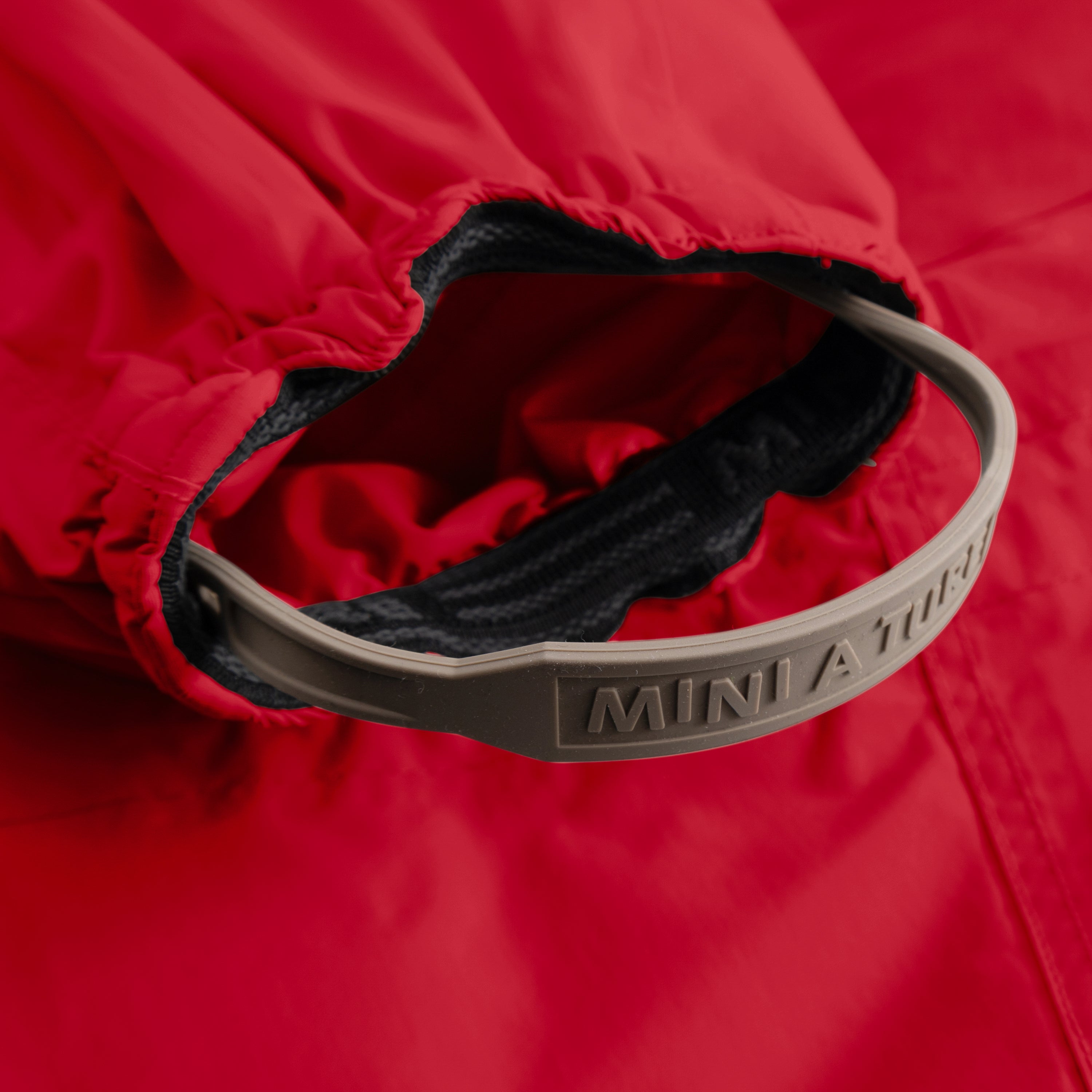 Detail of MATWISTI fleece lined snowsuit fur in bright red showing the internal adjustable waist with embossed MINI A TURE branding on the beige elastic strap, contrasting with the dark fleece lining and red waterproof outer shell.