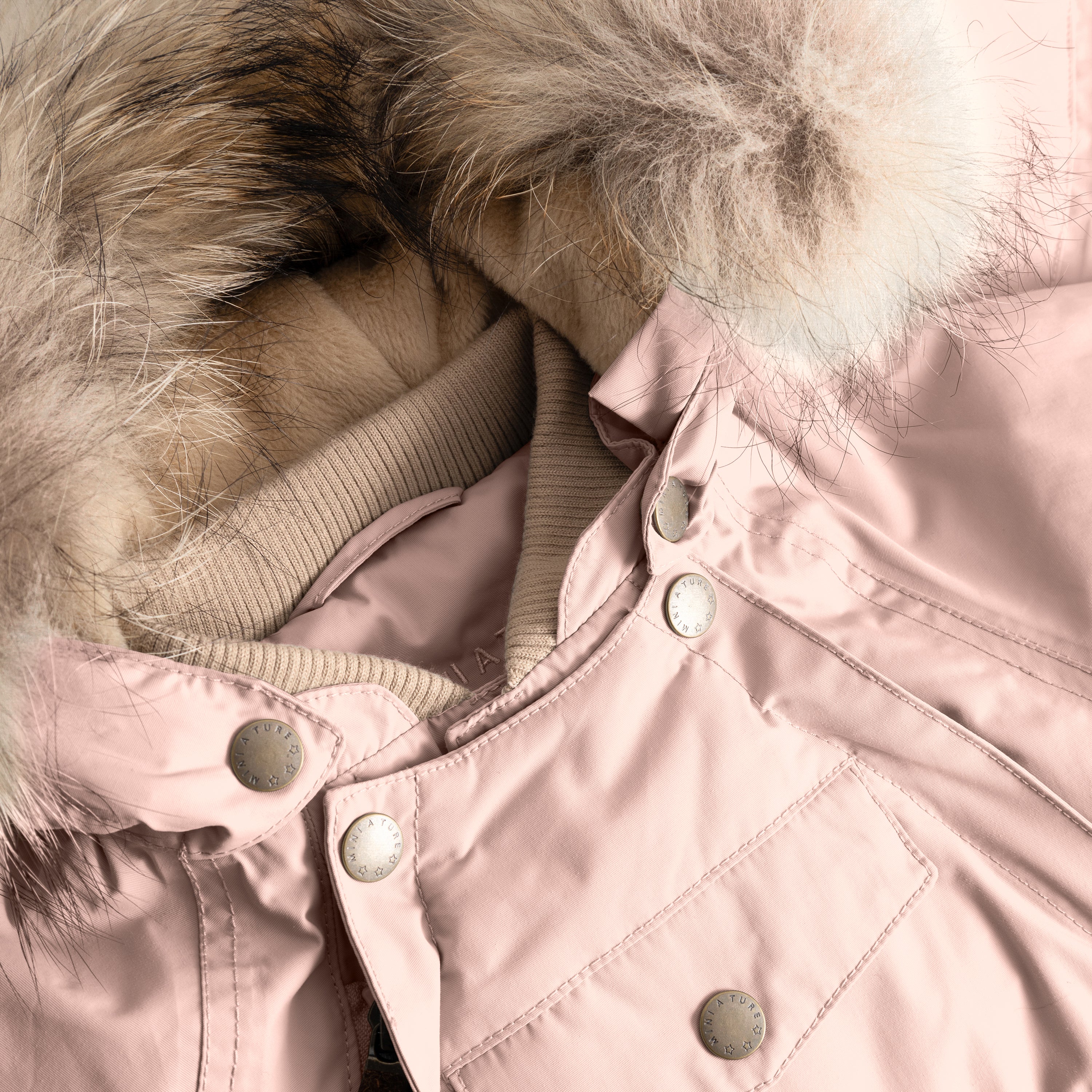 Close-up of MATWISTI fleece lined snowsuit fur in soft pink showing the detachable genuine fur hood trim, taupe ribbed collar, MINI A TURE branded press-stud fastenings along the chest, and front pocket detail on the waterproof shell.