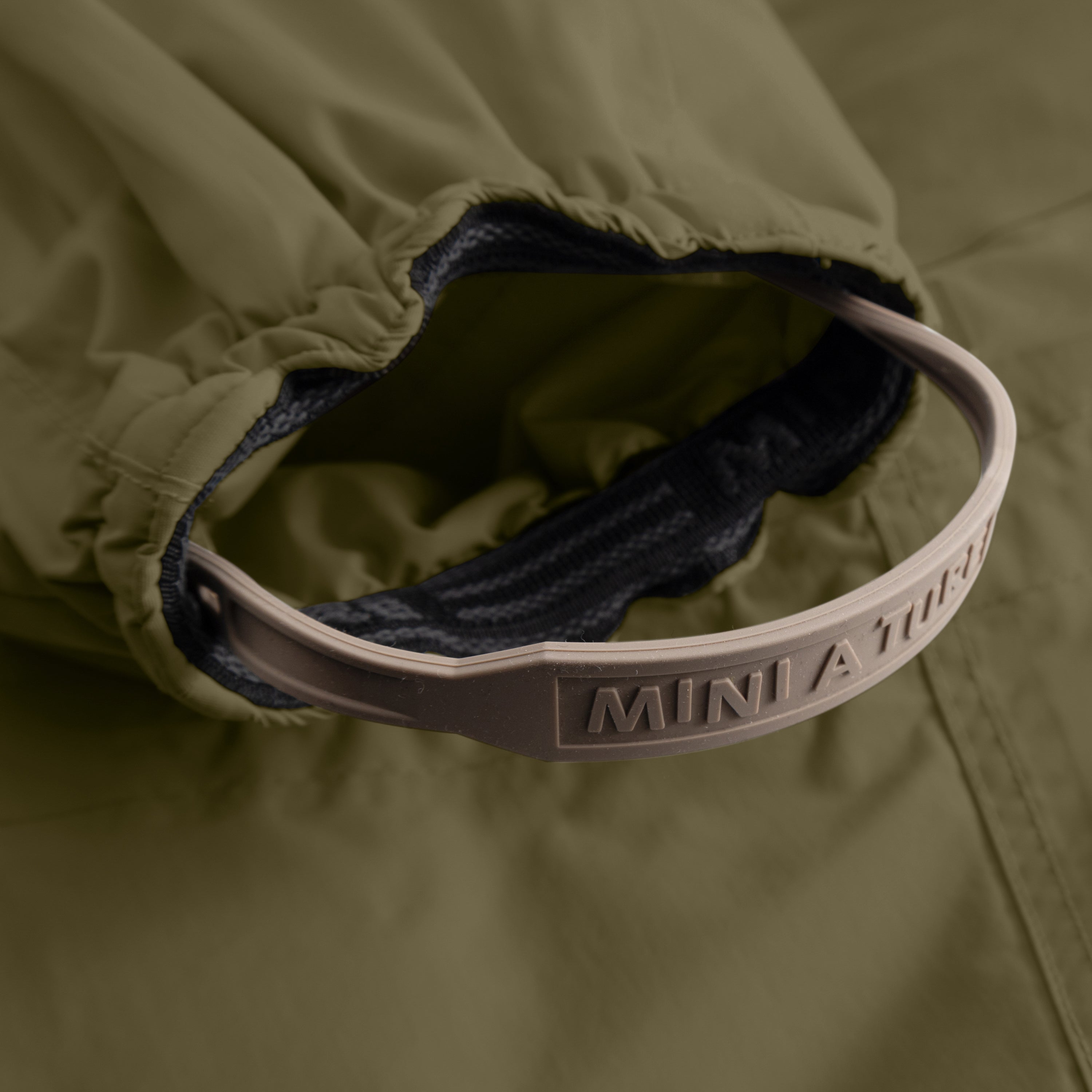 Detail of MATWISTI fleece lined snowsuit fur in olive green showing the internal adjustable waist with embossed MINI A TURE branding on the white elastic strap, contrasting with the dark fleece lining and olive waterproof outer shell.