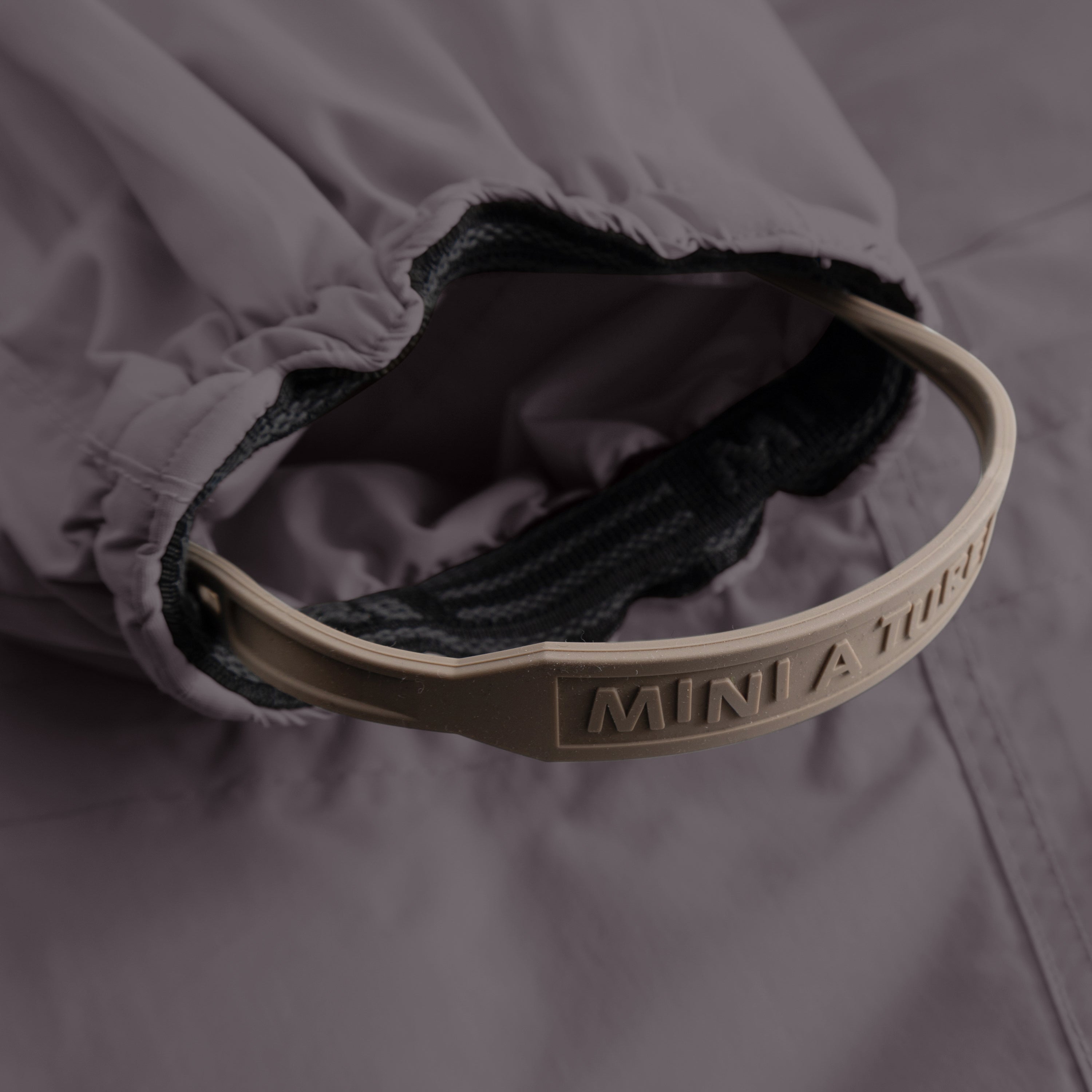 Close-up of MATWISTI fleece lined snowsuit fur in grey showing the internal adjustable waist with embossed MINI A TURE branding on the taupe silicone band, dark fleece lining visible inside, and elasticated construction.