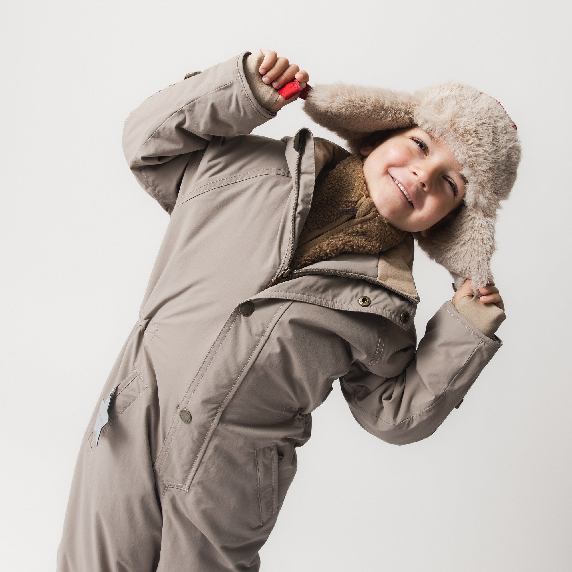 MATWANNI fleece lined snowsuit in light grey worn by a child with a faux-fur trimmed hat, showing the waterproof one-piece construction with two slanted front zips and a detachable hood.