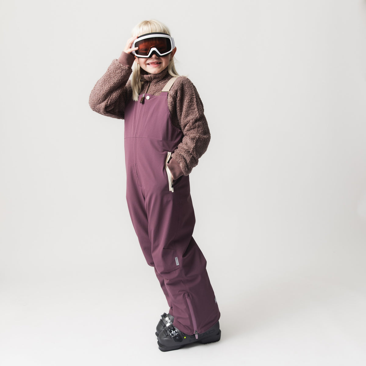 MATADAL Skihose in Altrosa, getragen von einem Kind mit Skibrille und braunem Fleecepullover, mit verstellbaren Trägern und seitlichen Reißverschlüssen am Beinende.