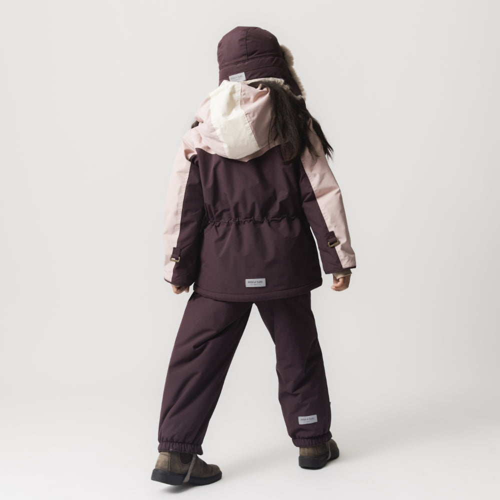 Child wearing the MATWALDO fleece lined winter jacket in deep plum and soft pink with matching waterproof trousers and a faux-fur trapper hat, shown from behind in a walking stance that demonstrates the jacket's adjustable internal waist, snow cuffs and freedom of movement during cold-weather wear.
