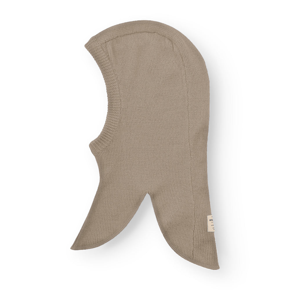 MATKEA light balaclava in taupe merino wool, shown flat to illustrate the elongated neck flaps that drape over the shoulders and the central face opening designed for layering beneath winter outerwear.
