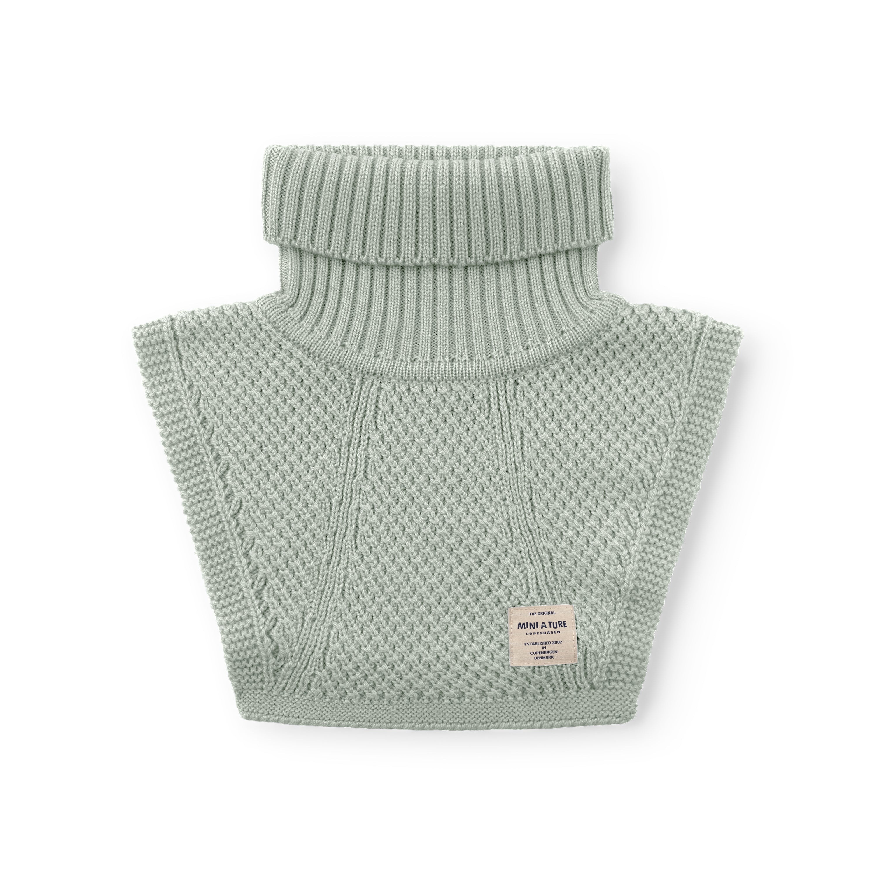 MATTAYLER neckwarmer in pale sage green merino wool, laid flat against a white background, displaying the wide ribbed high neck and moss-stitch textured body with a rectangular MINI A TURE label positioned at the lower right of the front panel.