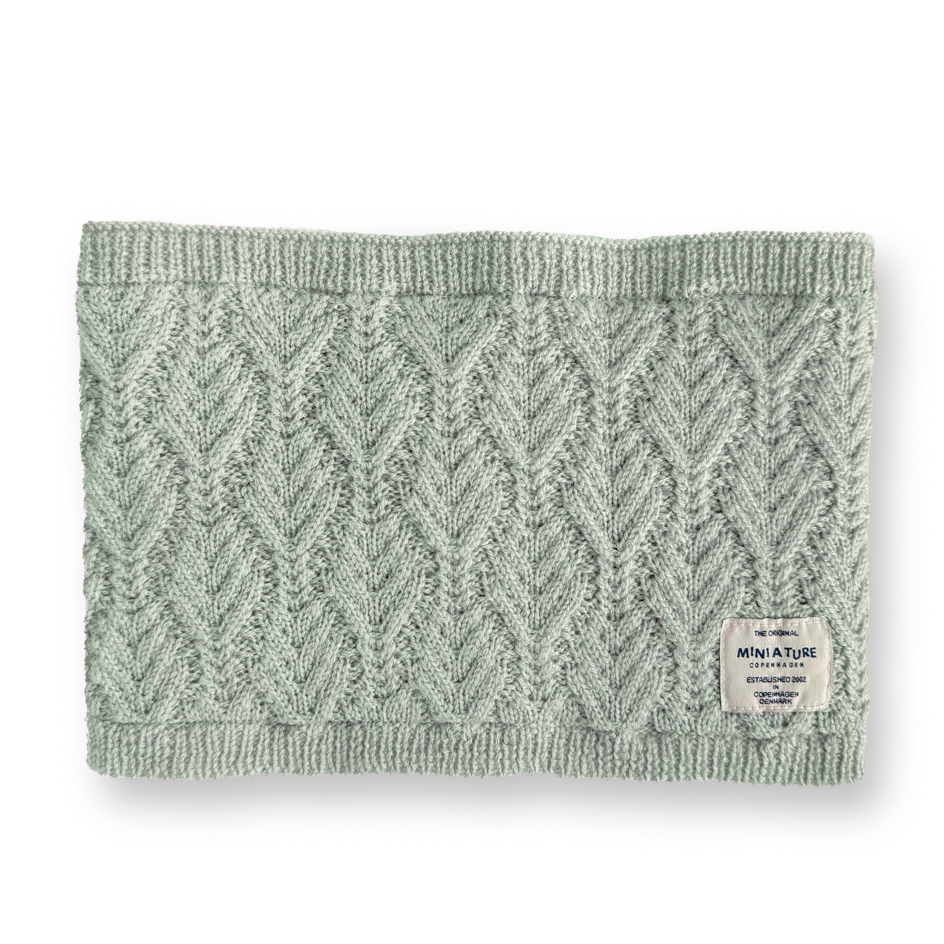 MATGOI fleece lined neckwarmer laid flat showing the textured herringbone knit outer in pale sage merino wool with ribbed edges and a MINI A TURE woven label at the lower right corner.