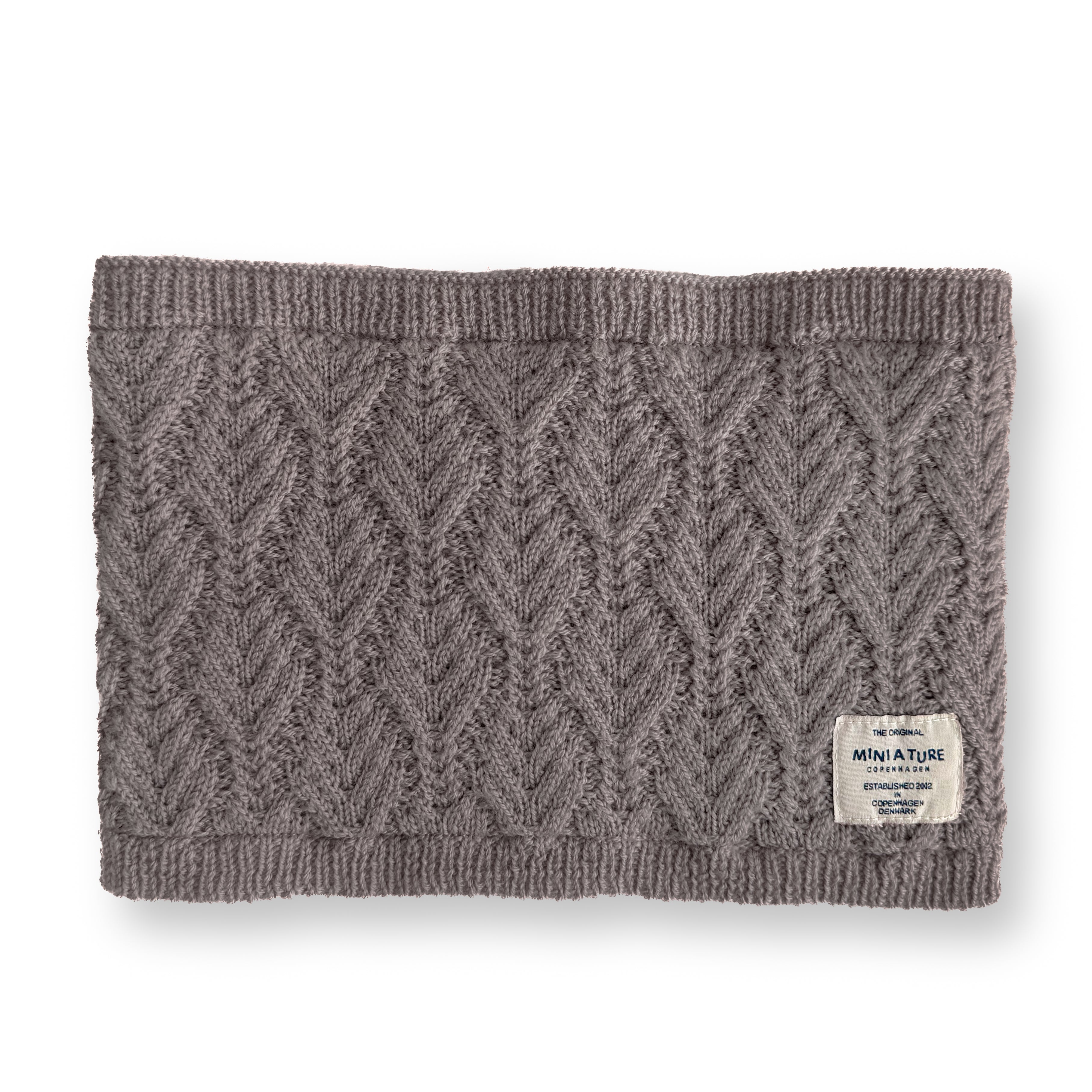 MATGOI fleece lined neckwarmer in warm taupe merino wool with chevron knit texture, ribbed top and bottom edges, and a cream MINI A TURE woven label at the lower right corner.