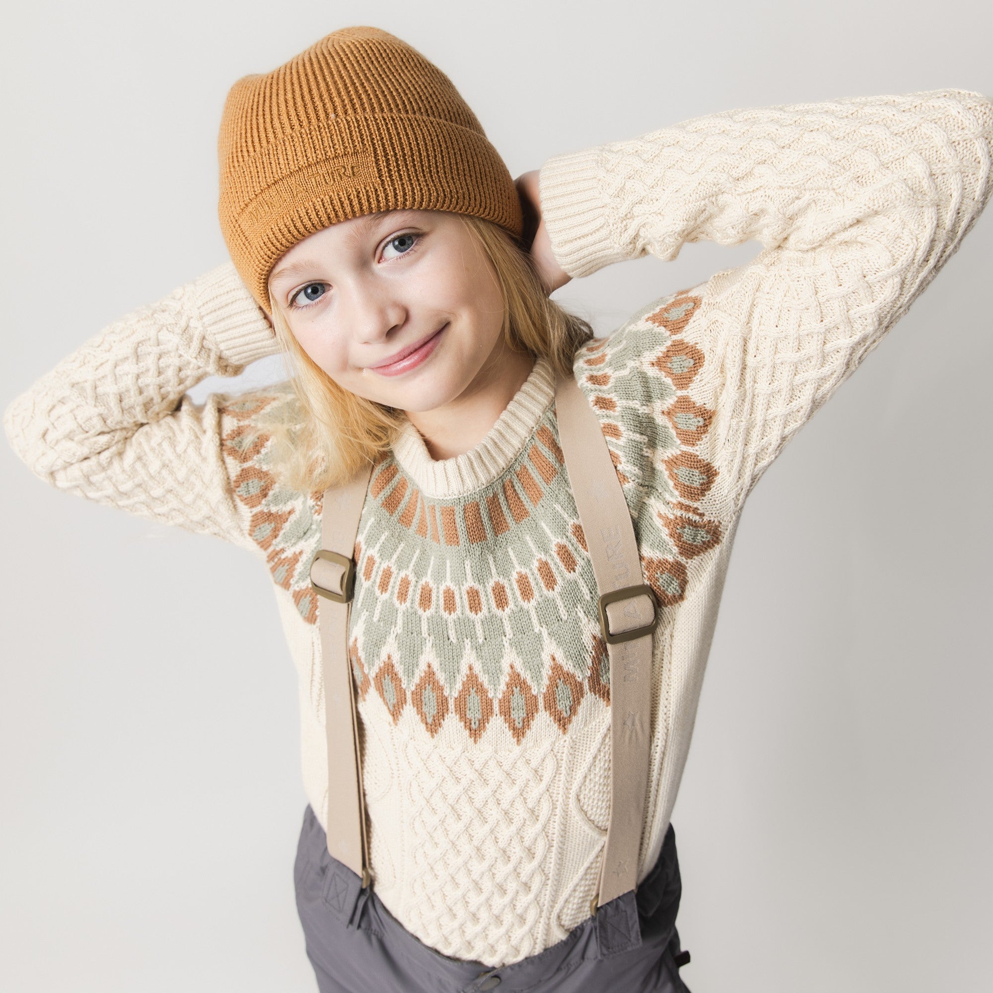 MATBOJE beanie in camel-coloured merino wool with a ribbed knit and fold-up brim, worn by a child in a patterned cream jumper.