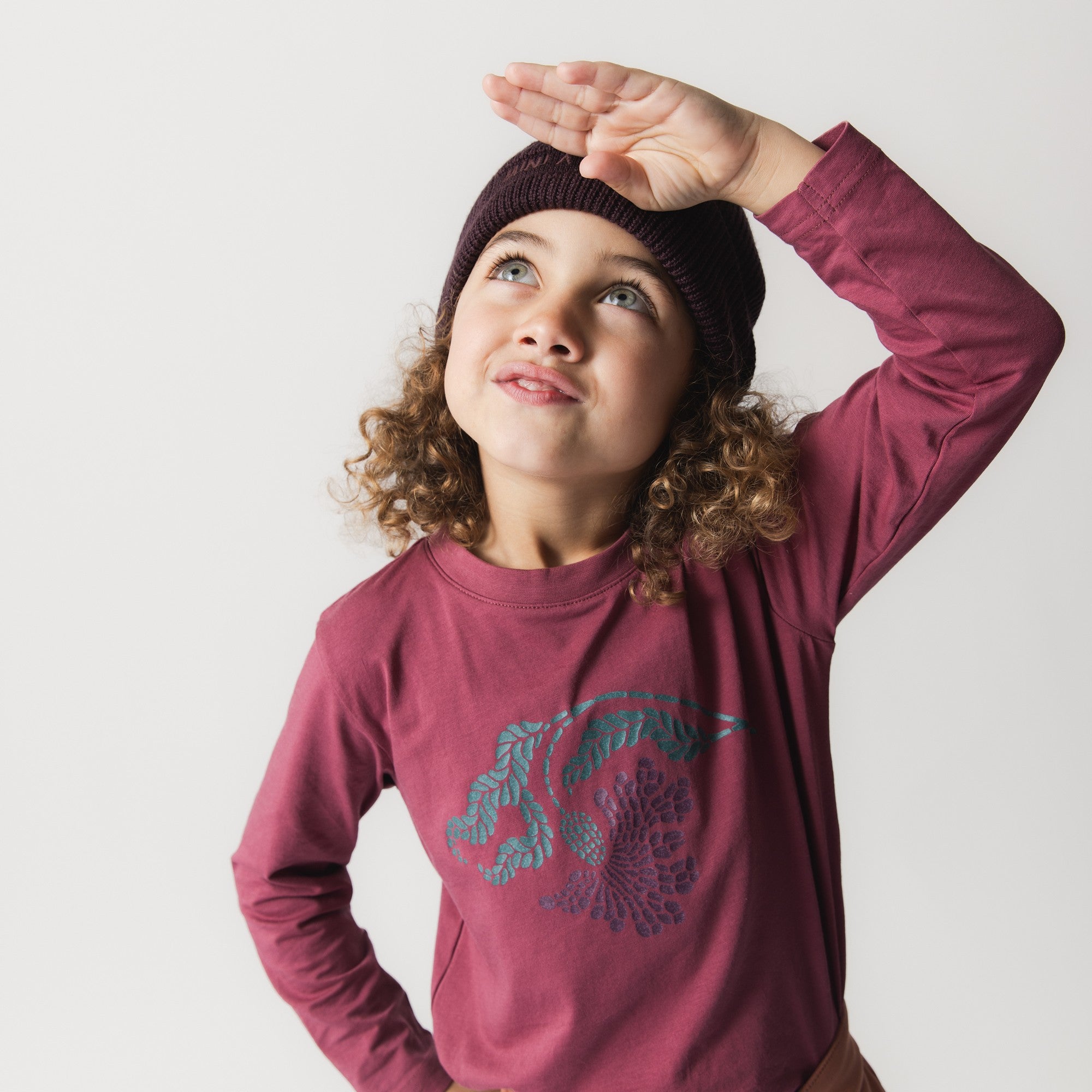 MATBOJE beanie in deep plum merino wool with a ribbed knit, worn by a child in a burgundy long-sleeve top who is shielding their eyes while looking upward.