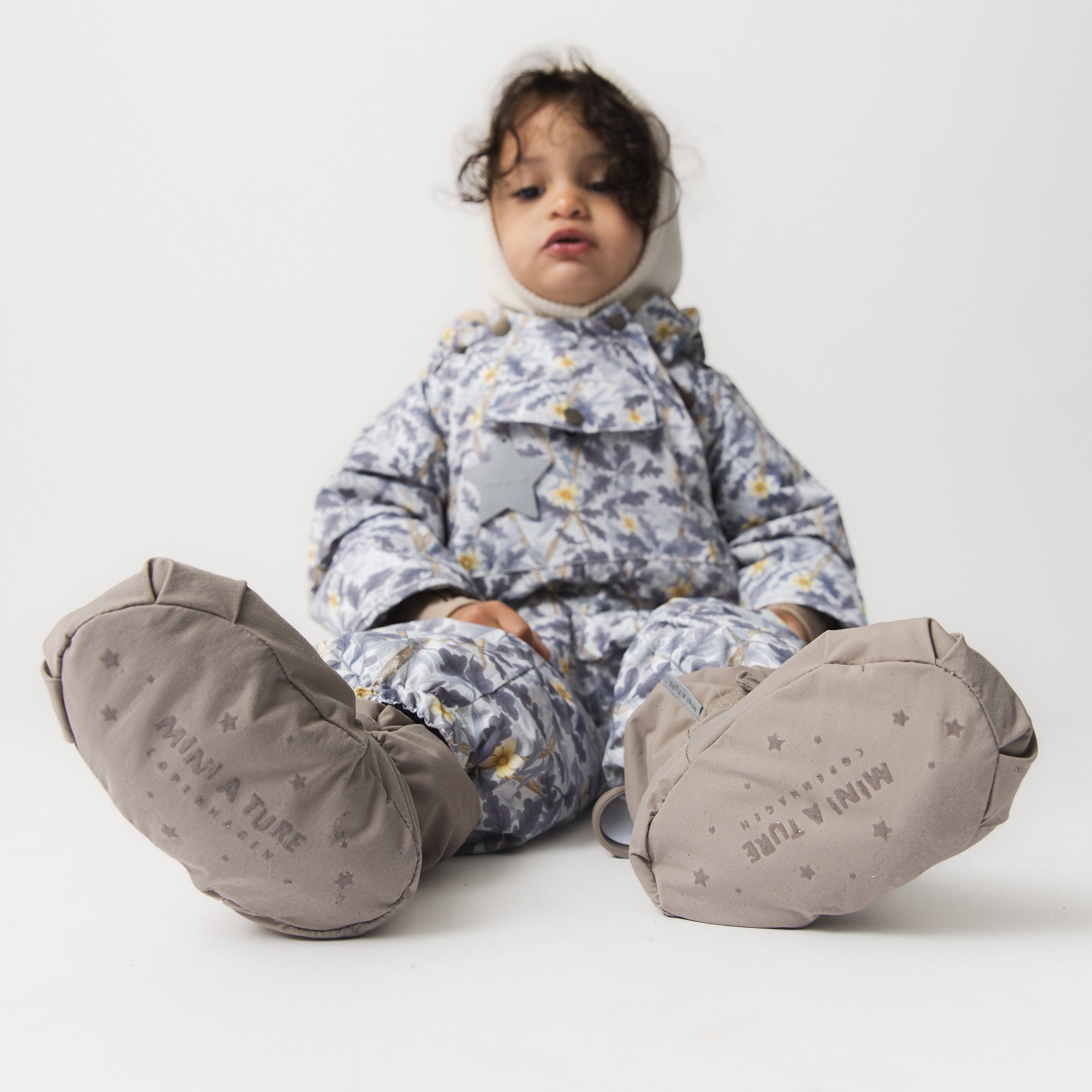 MATWINN fleece lined winter outdoor sock in taupe grey with star pattern and adjustable velcro ankle strap, worn by a toddler in a floral snowsuit during a studio session.