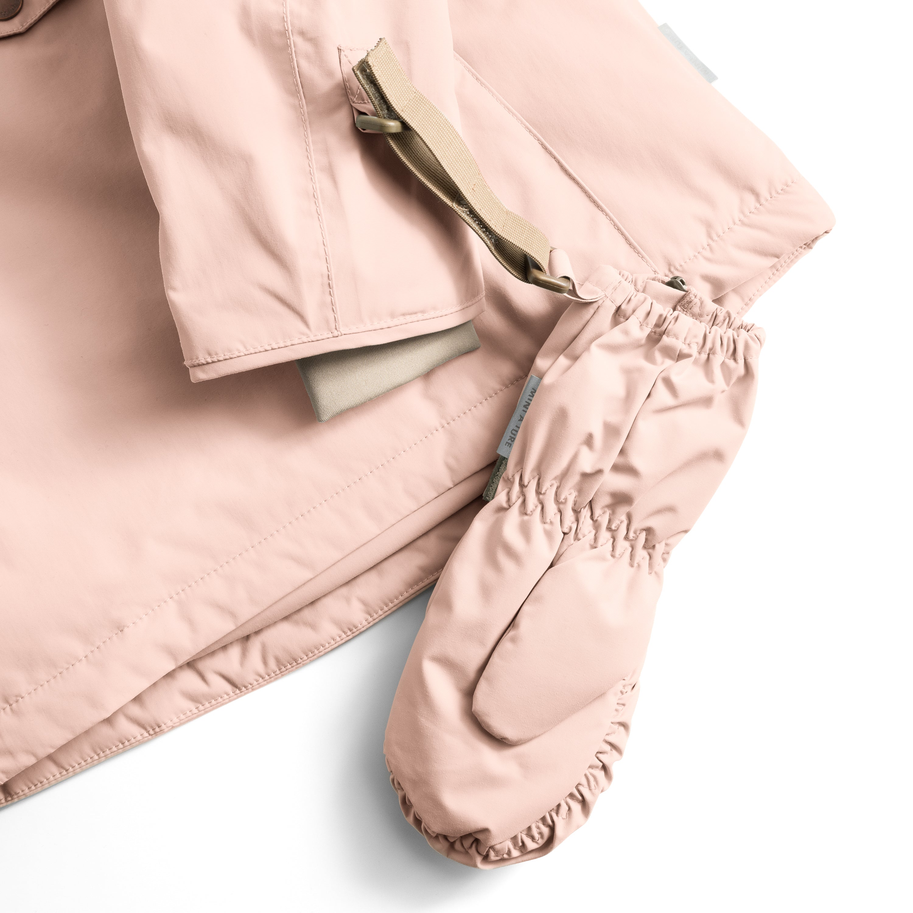 MATCESAR mitten in soft blush pink shown with the full-length front zip partially open, displaying the soft fleece lining and elastic gathered cuff, with the beige webbing strap threaded through the wrist loop and visible against the smooth recycled polyamide shell.
