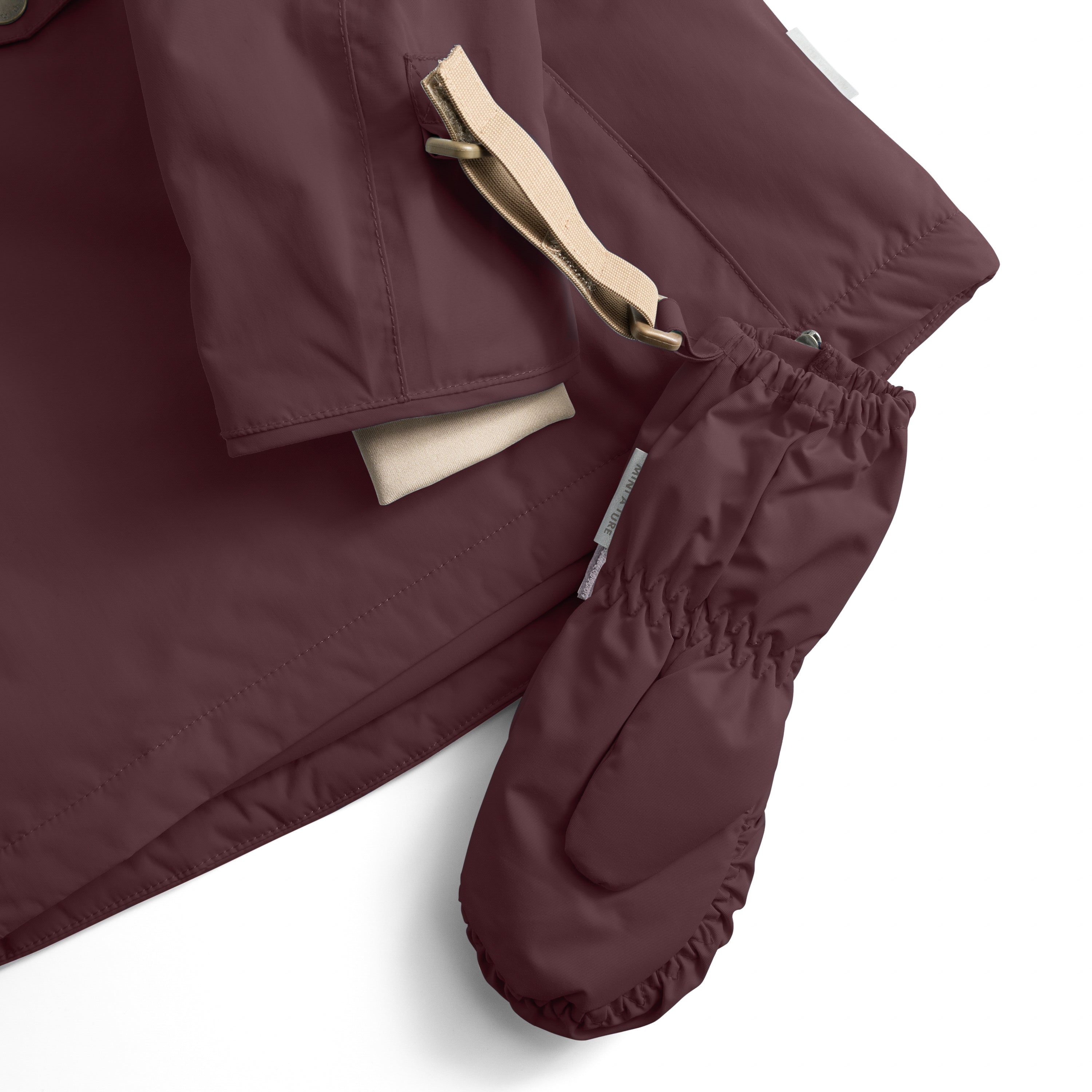 Close-up detail of MATCESAR mittens showing the beige webbing strap threaded through a fabric loop at the wrist, elastic cuffs with MINI A TURE branding, and the soft fleece lining visible at the cuff opening.
