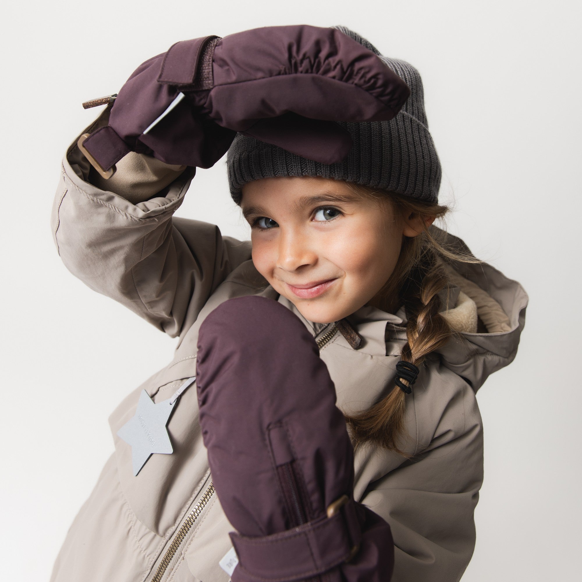 MATCESAR fleece-lined mittens in plum with front zip and adjustable wrist strap, worn by a child in a beige winter jacket and dark knitted beanie.