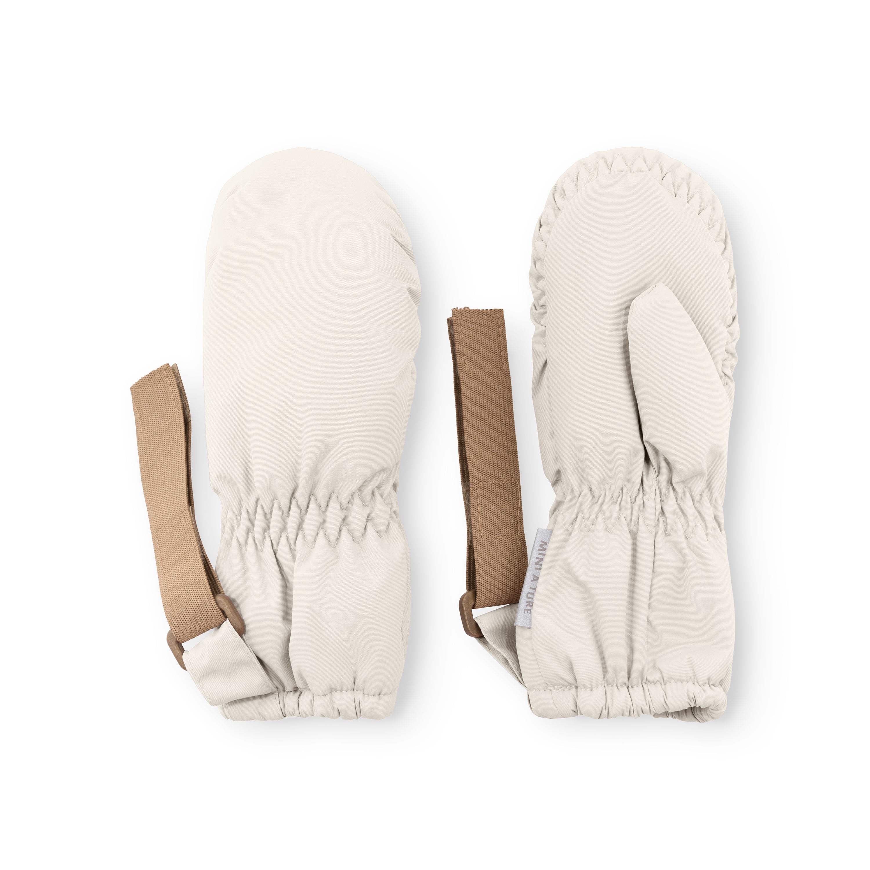 MATCORDT fleece lined mittens in pale cream displayed flat on a white background, showing both the waterproof outer shell and palm side with elastic gathered cuffs at the wrist and top, alongside the extended beige velcro attachment straps and a visible MINI A TURE care label.