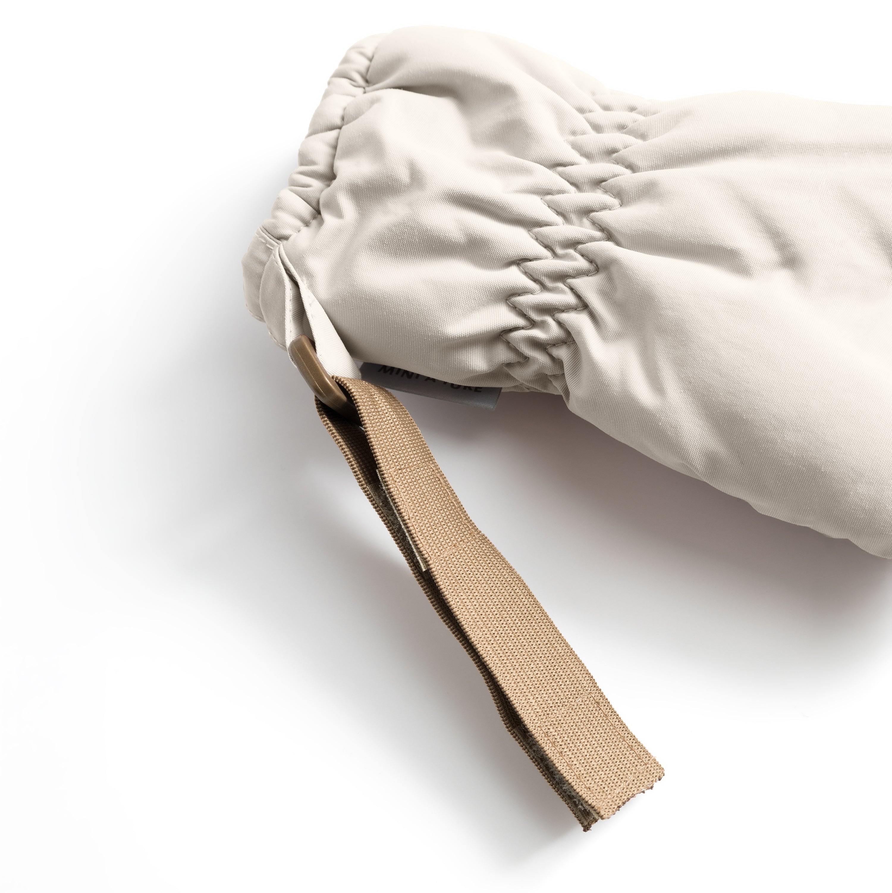MATCORDT fleece lined mittens in pale cream shown in close-up, highlighting the elastic gathered wrist construction that seals out draughts, the extended beige velcro attachment strap and the waterproof recycled polyamide shell with visible stitching detail.