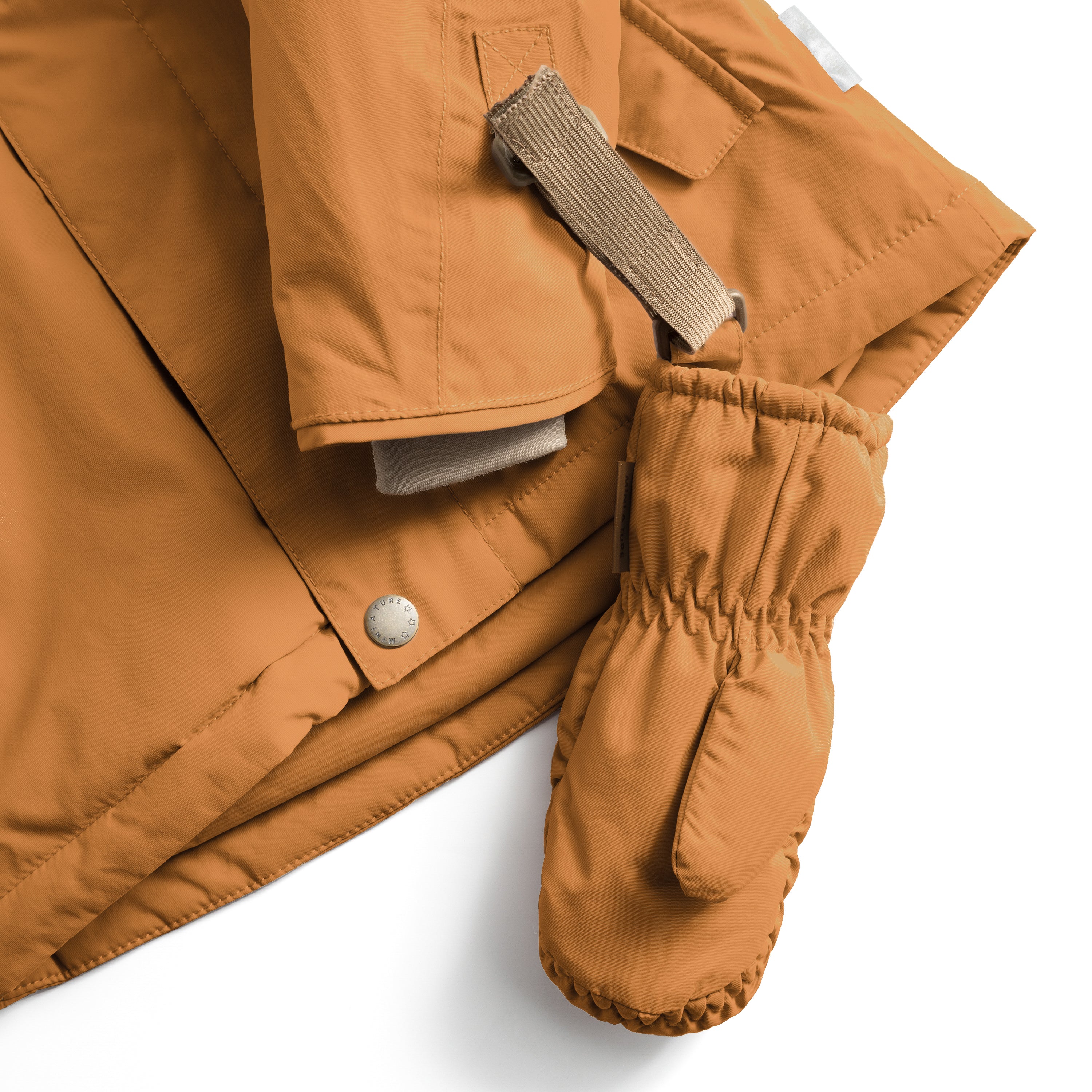 MATCORDT fleece lined mittens in caramel brown shown attached to a matching jacket via the beige velcro strap and D-loop, with the elastic gathered cuff visible at the wrist and the waterproof recycled polyamide shell demonstrating the secure fastening system designed to prevent loss during transitions.
