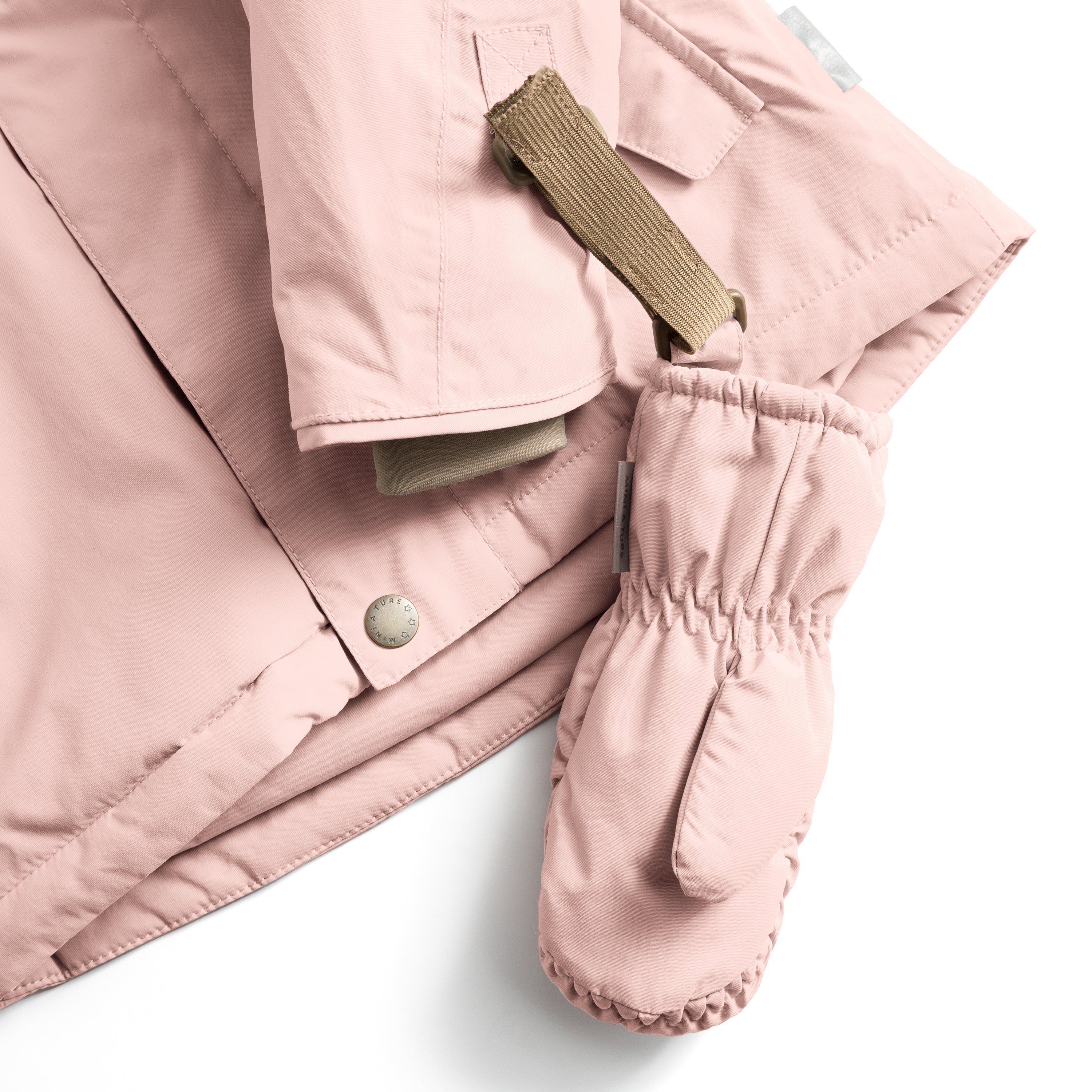 MATCORDT fleece lined mittens in pale pink shown attached to a matching jacket via the beige velcro strap and D-loop, with the elastic gathered cuff visible at the wrist and the waterproof recycled polyamide shell demonstrating how the fastening system keeps mittens secured to outerwear during transitions.