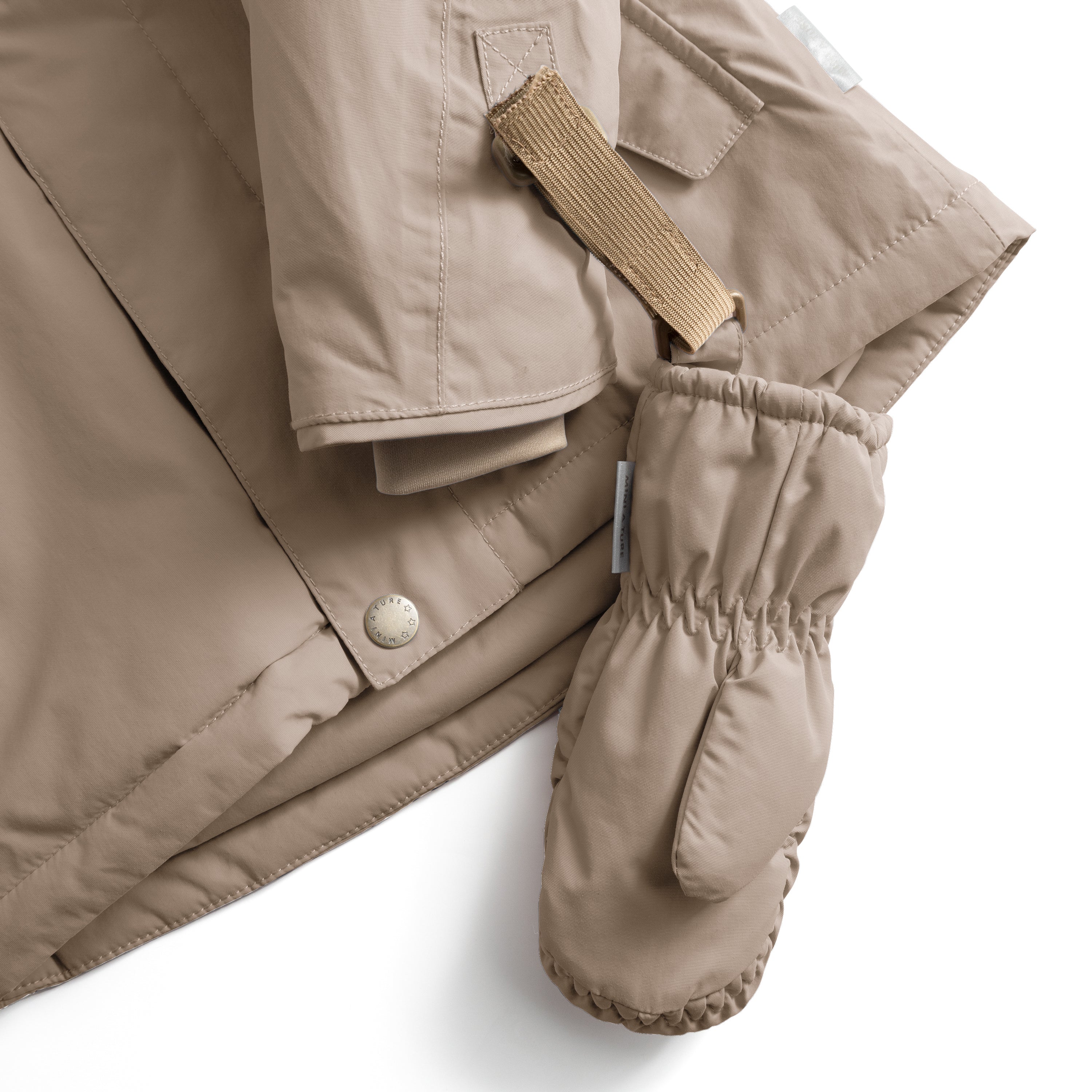 MATCORDT fleece lined mittens in warm beige shown attached to a matching jacket via the beige velcro strap threaded through the triangular D-loop tab, with the elastic gathered cuff creating a secure seal at the wrist and a press-stud jacket closure visible alongside the waterproof recycled polyamide shell.