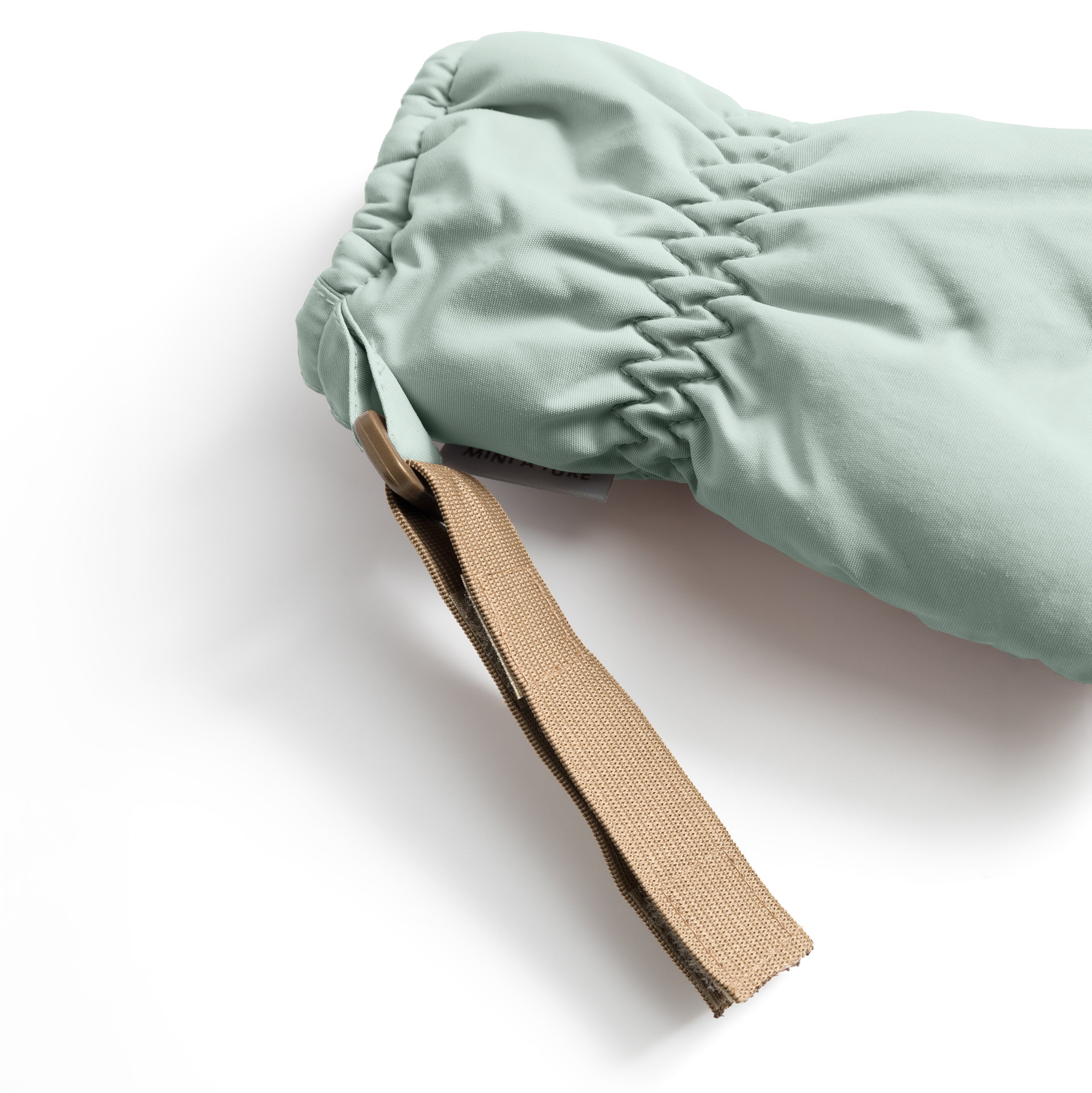 MATCORDT fleece lined mittens in pale mint green shown in close-up from the cuff, with the elastic gathered wrist construction visible alongside the extended beige velcro attachment strap and a glimpse of the soft fleece lining at the opening.