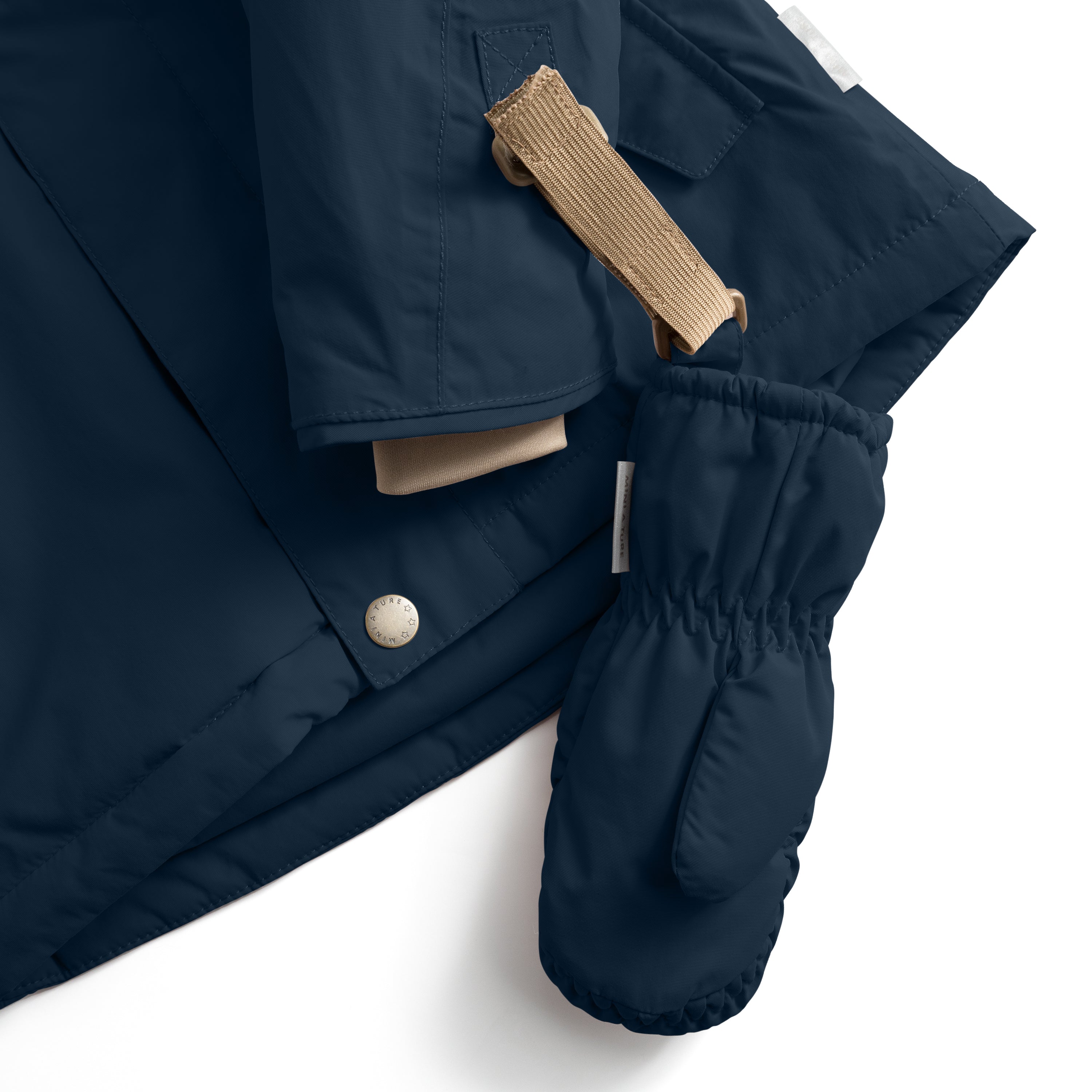 MATCORDT fleece lined mittens in navy blue shown in close-up detail, with the beige velcro attachment strap threaded through a D-loop on a matching jacket, demonstrating the secure fastening system that keeps mittens attached to outerwear during transitions, alongside the elastic gathered cuff and press-stud jacket closure.