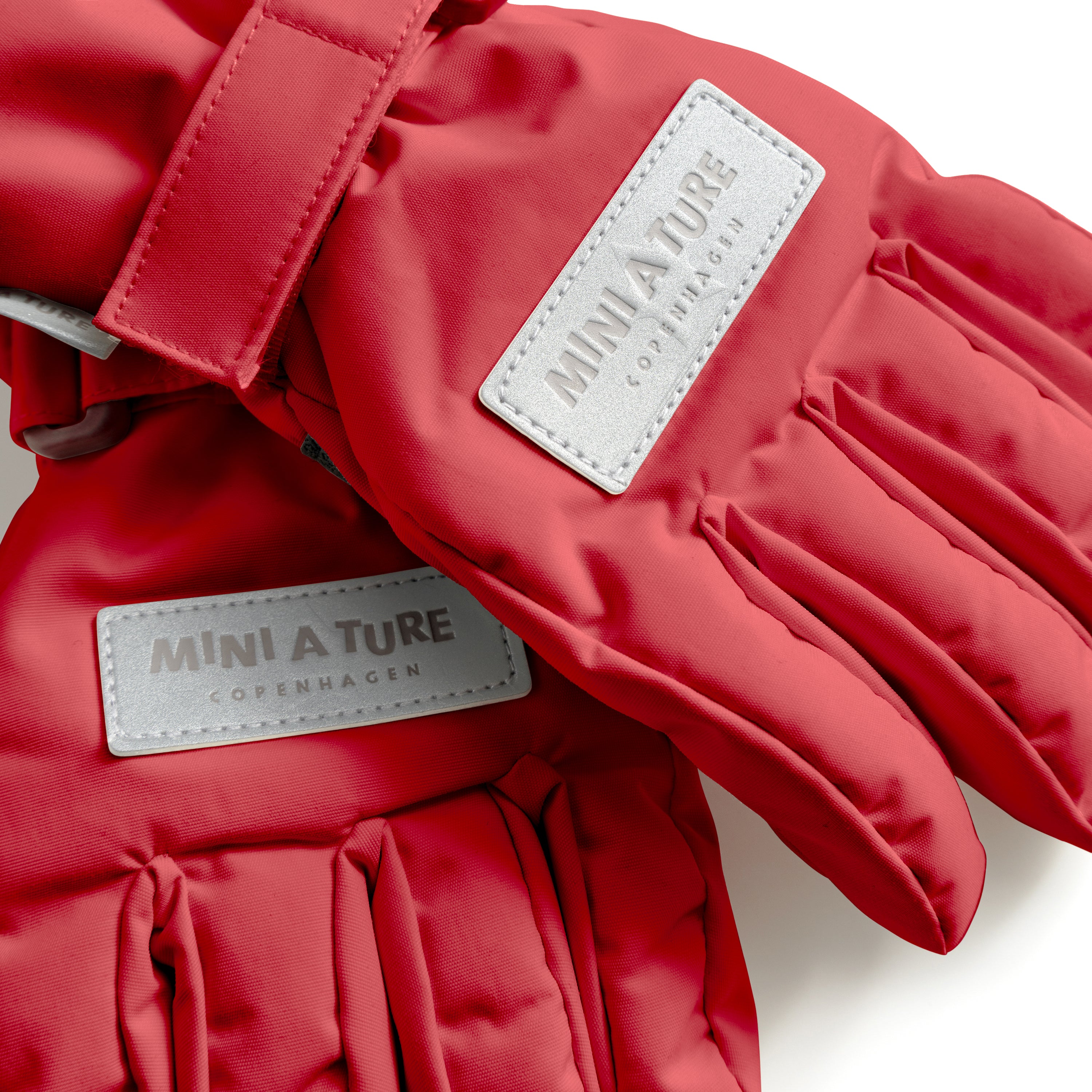 MATCELIO gloves in red with embossed MINI A TURE Copenhagen labels on both the back of hand and extended cuff, photographed flat to show the waterproof recycled nylon outer shell, THERMOLITE padding and adjustable wrist strap with buckle closure.